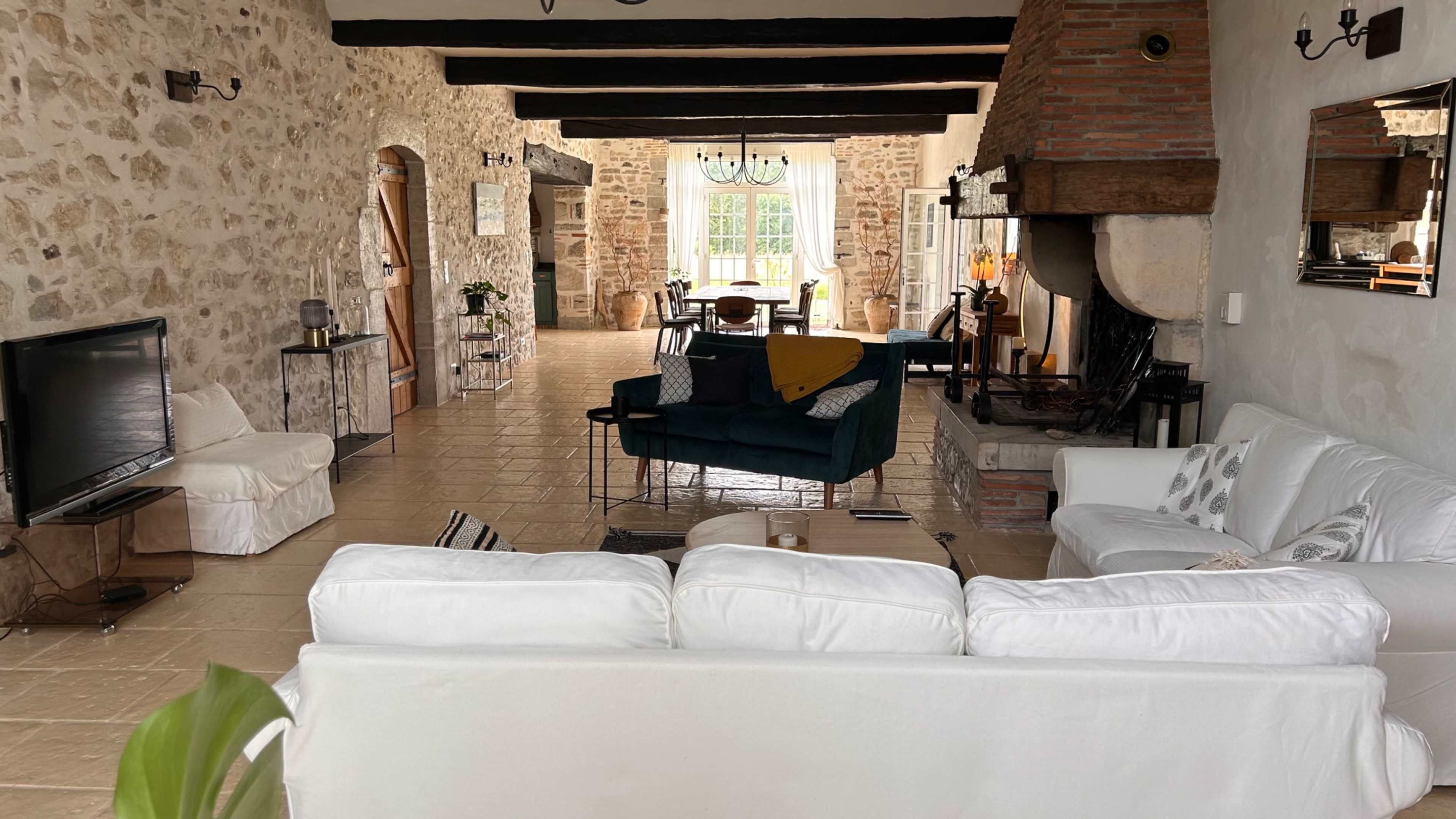 A spacious, rustic living area with stone walls, wooden beams, and a cozy seating arrangement centered around a fireplace.