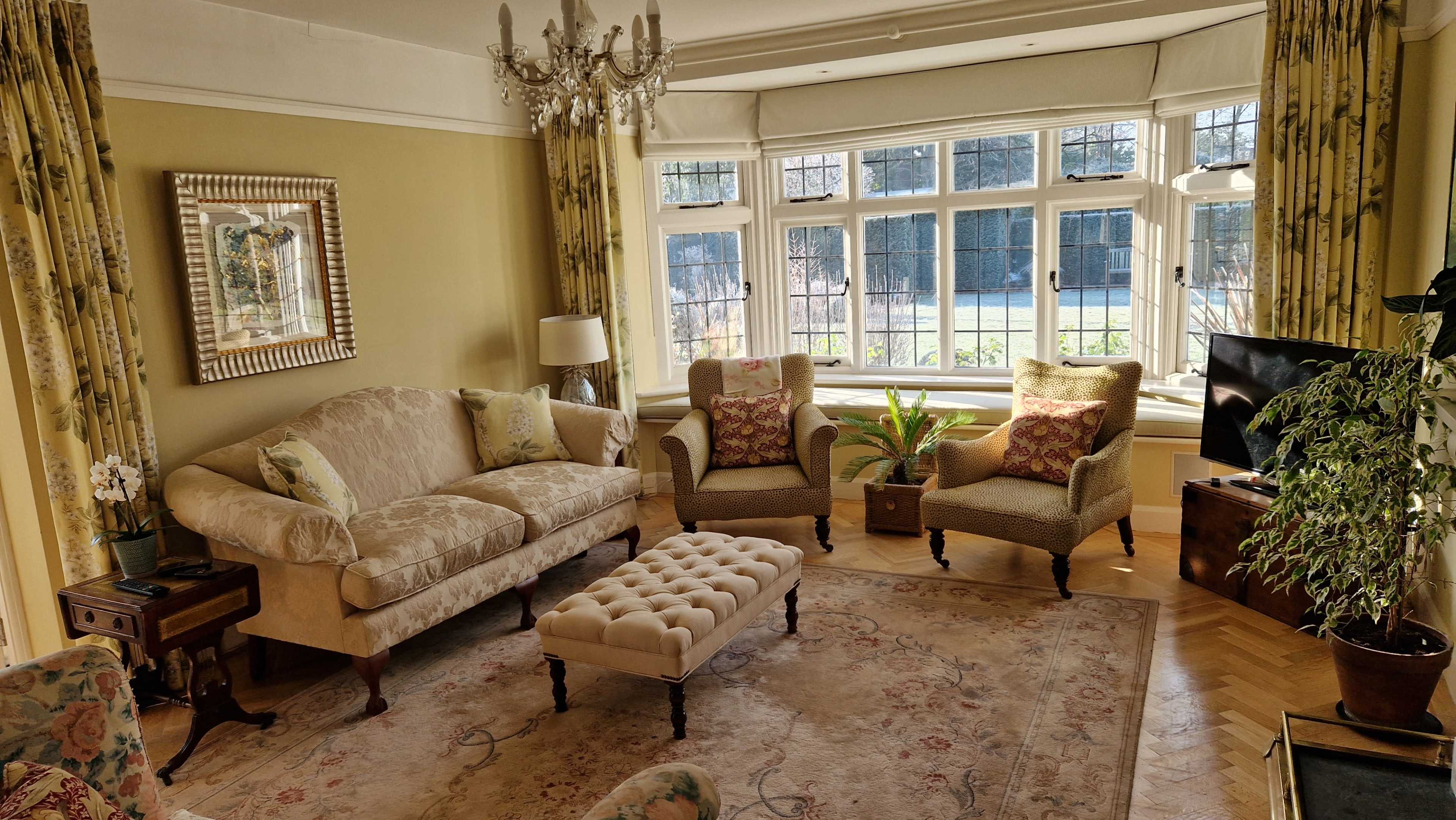 A well-furnished living room with a sofa, two armchairs, a decorative coffee table, and large windows letting in natural light.