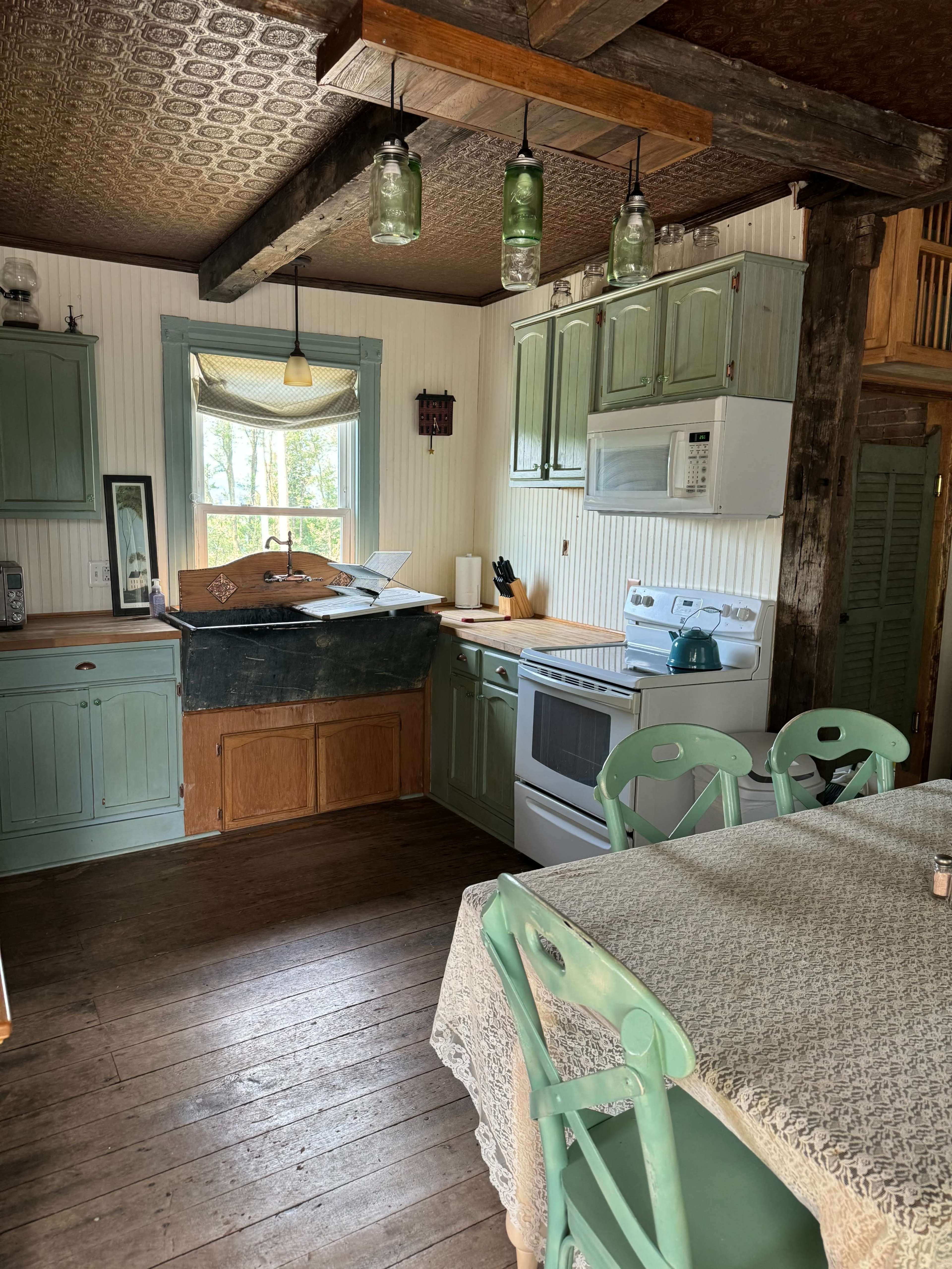 A rustic kitchen with green cabinets, a wooden table, and a window that lets in natural light.