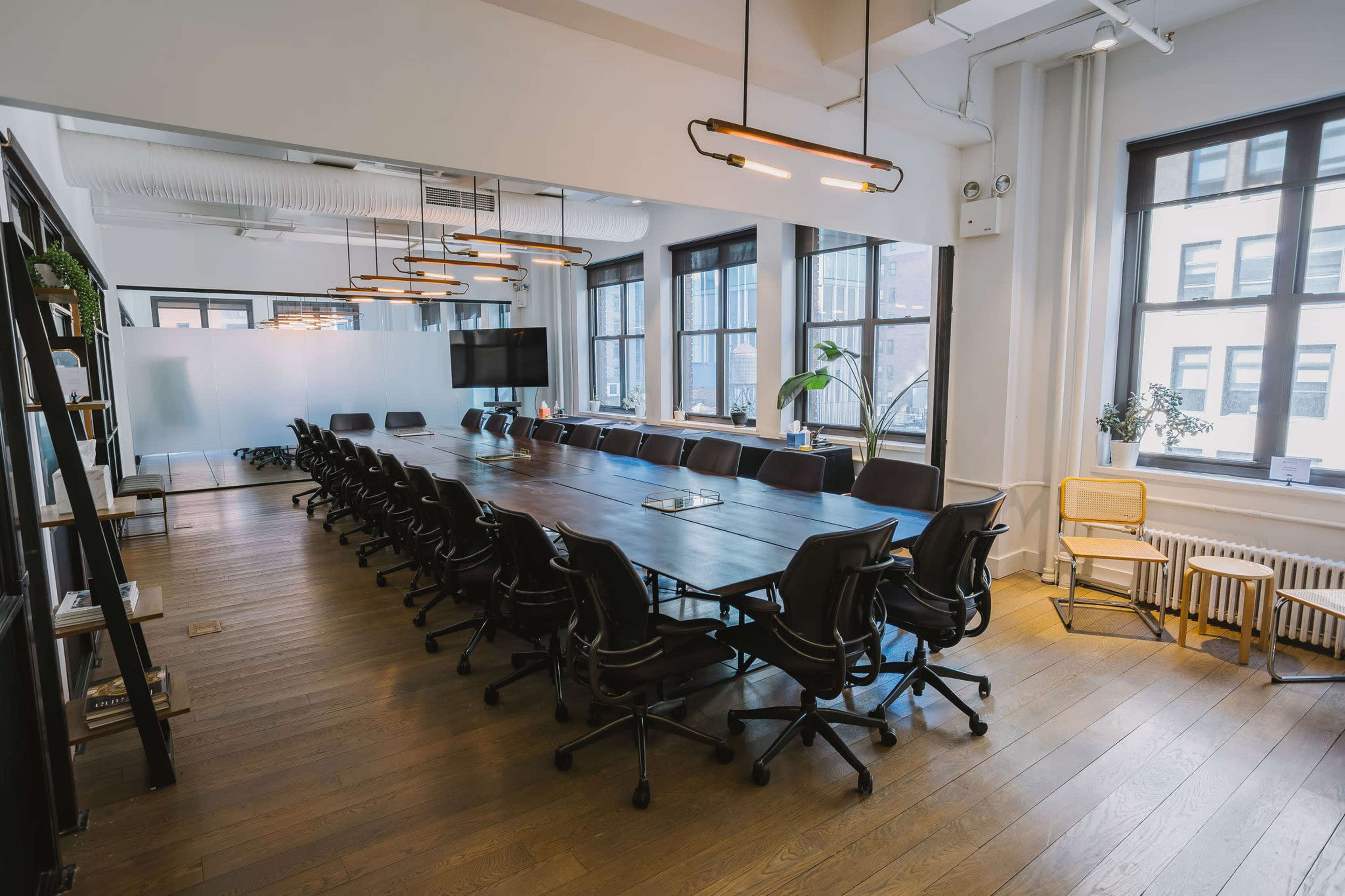 A spacious conference room features a large table surrounded by ergonomic chairs, with windows providing ample natural light.