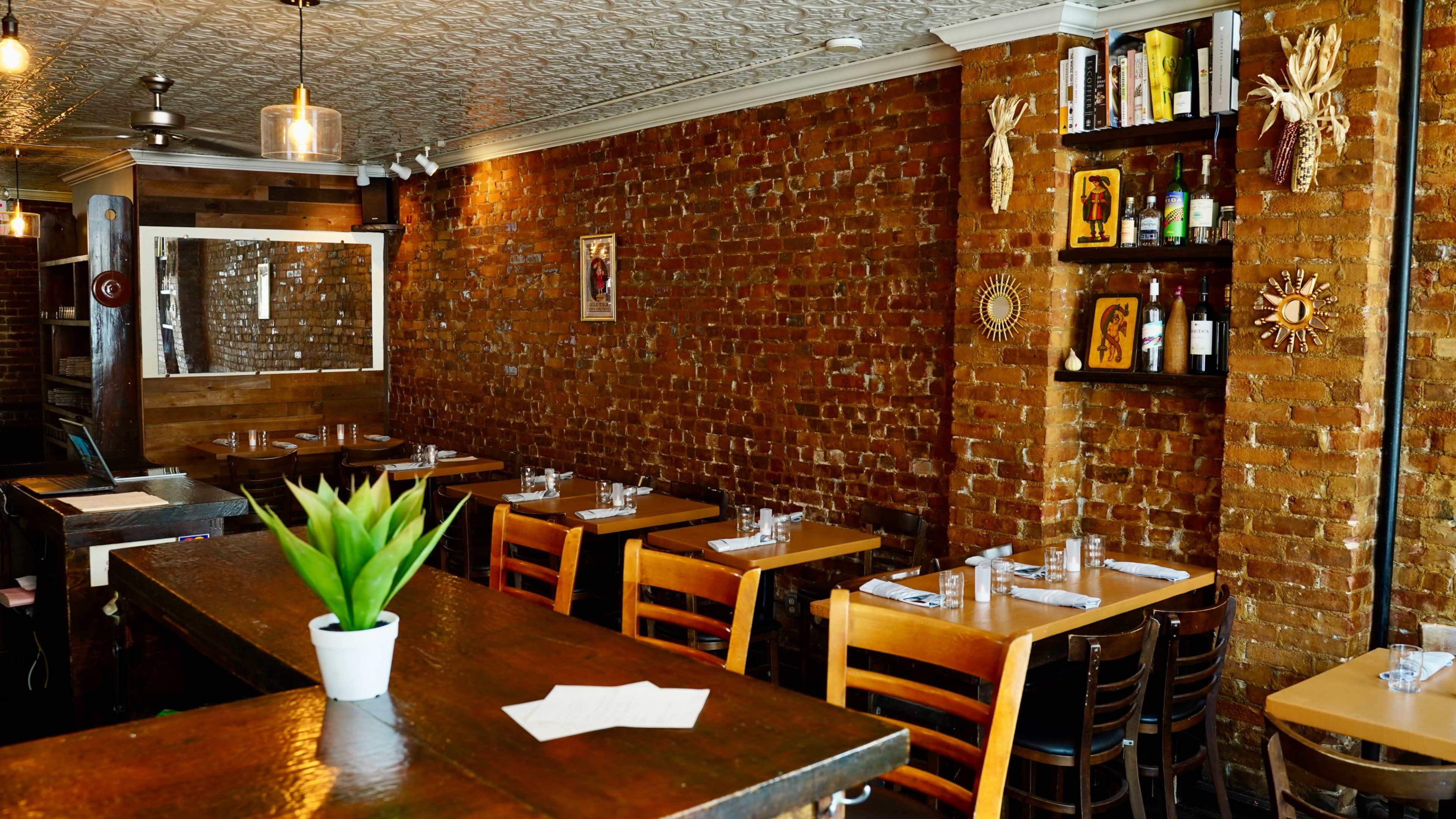 The image shows a cozy restaurant interior with brick walls, wooden tables, and shelves displaying various decor items and bottles.