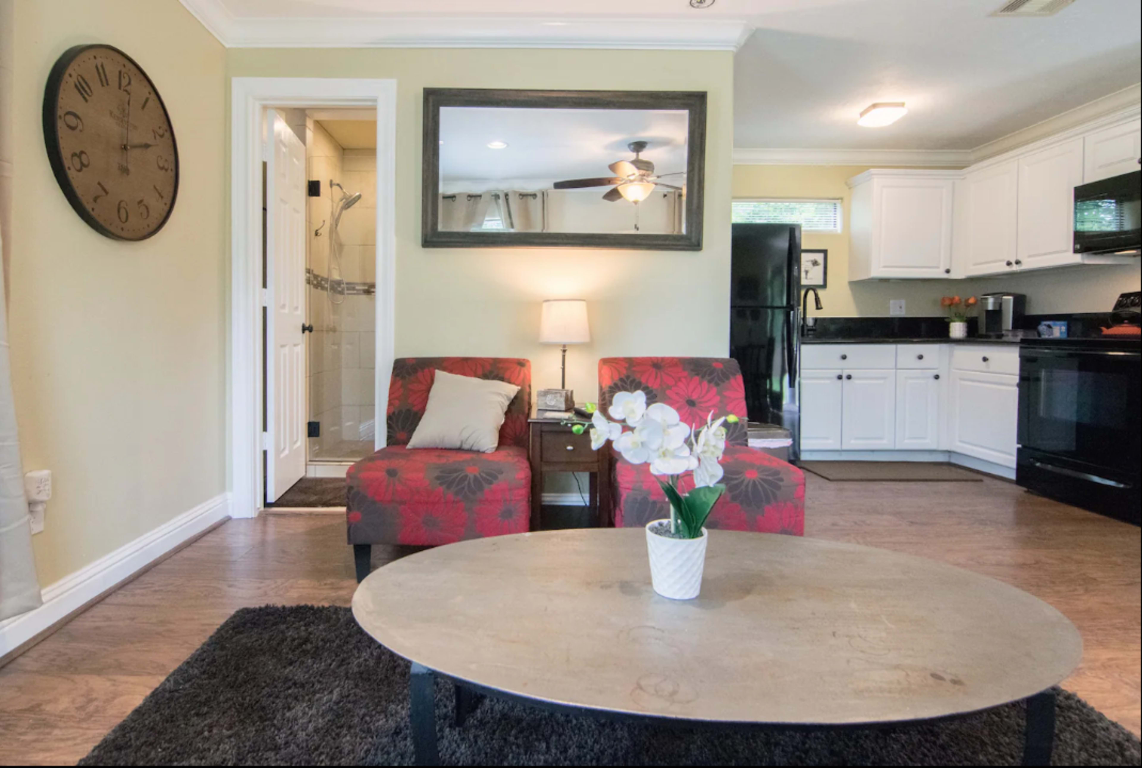 A living space featuring two red chairs, a round coffee table, and a kitchen area with black appliances and white cabinets.