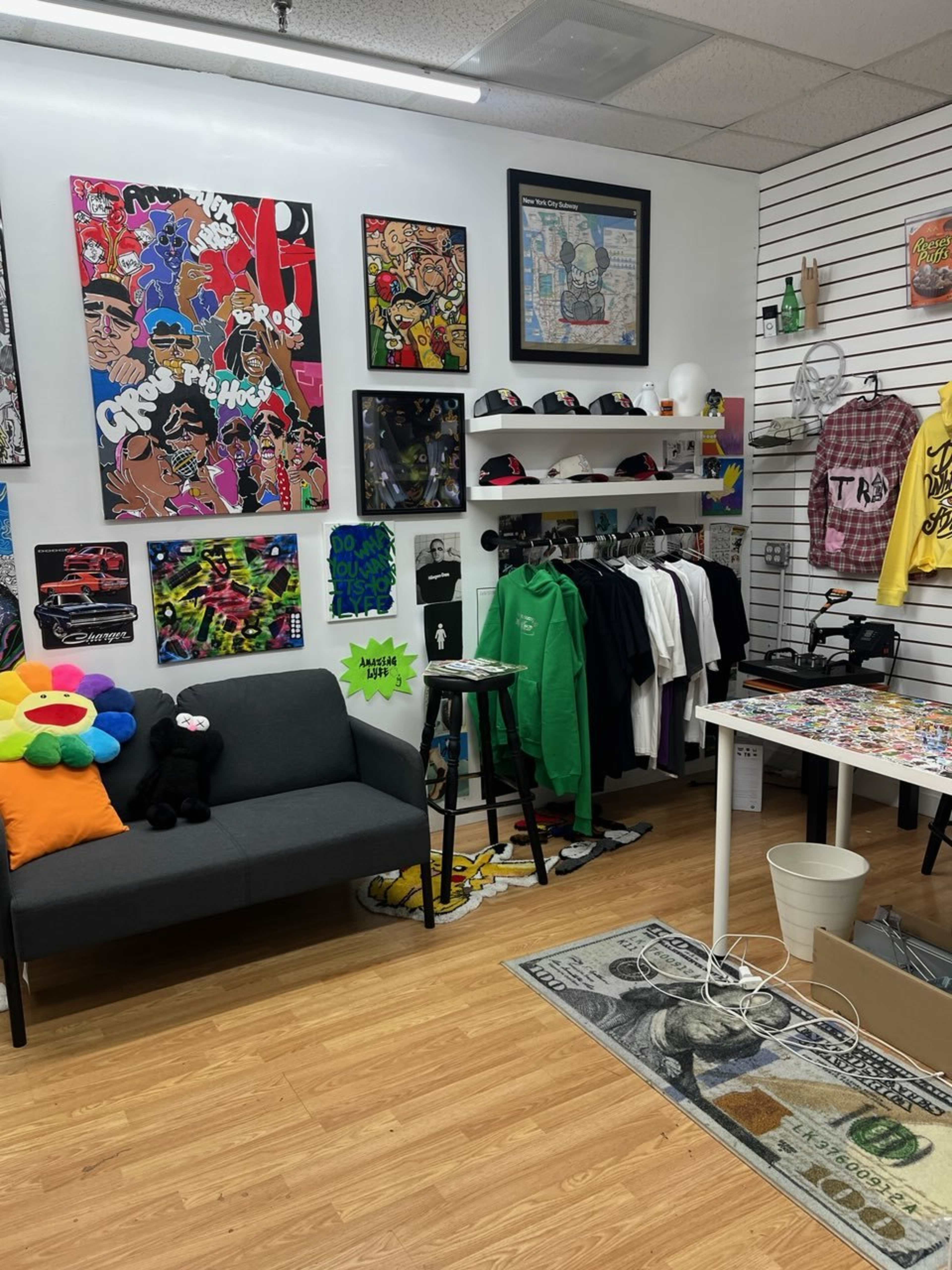 The image shows a boutique featuring colorful artwork on the walls, a variety of clothing on display, and a cozy seating area with plush toys.