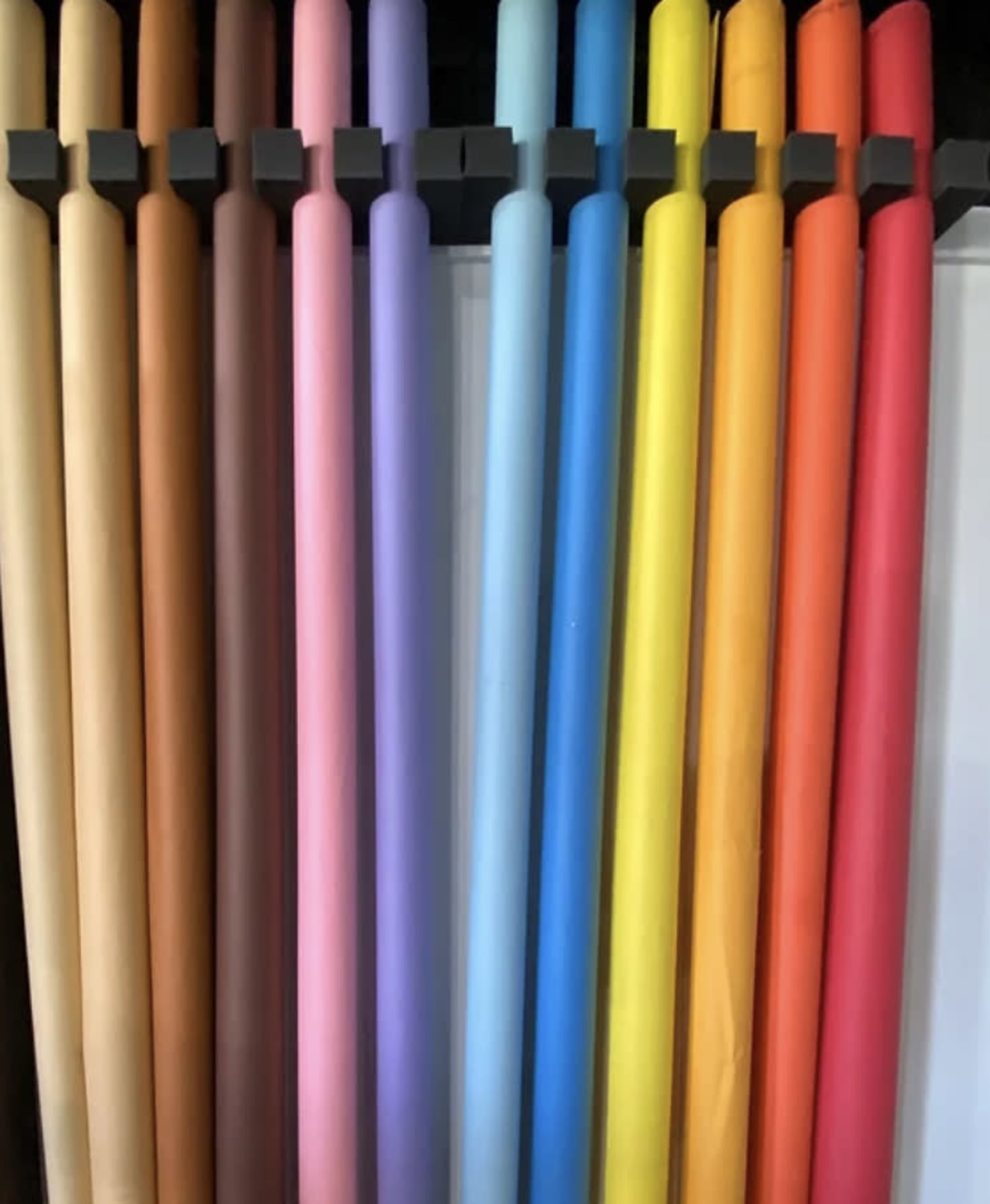 The image shows a row of rolled paper sheets in various colors, neatly arranged on a rack.