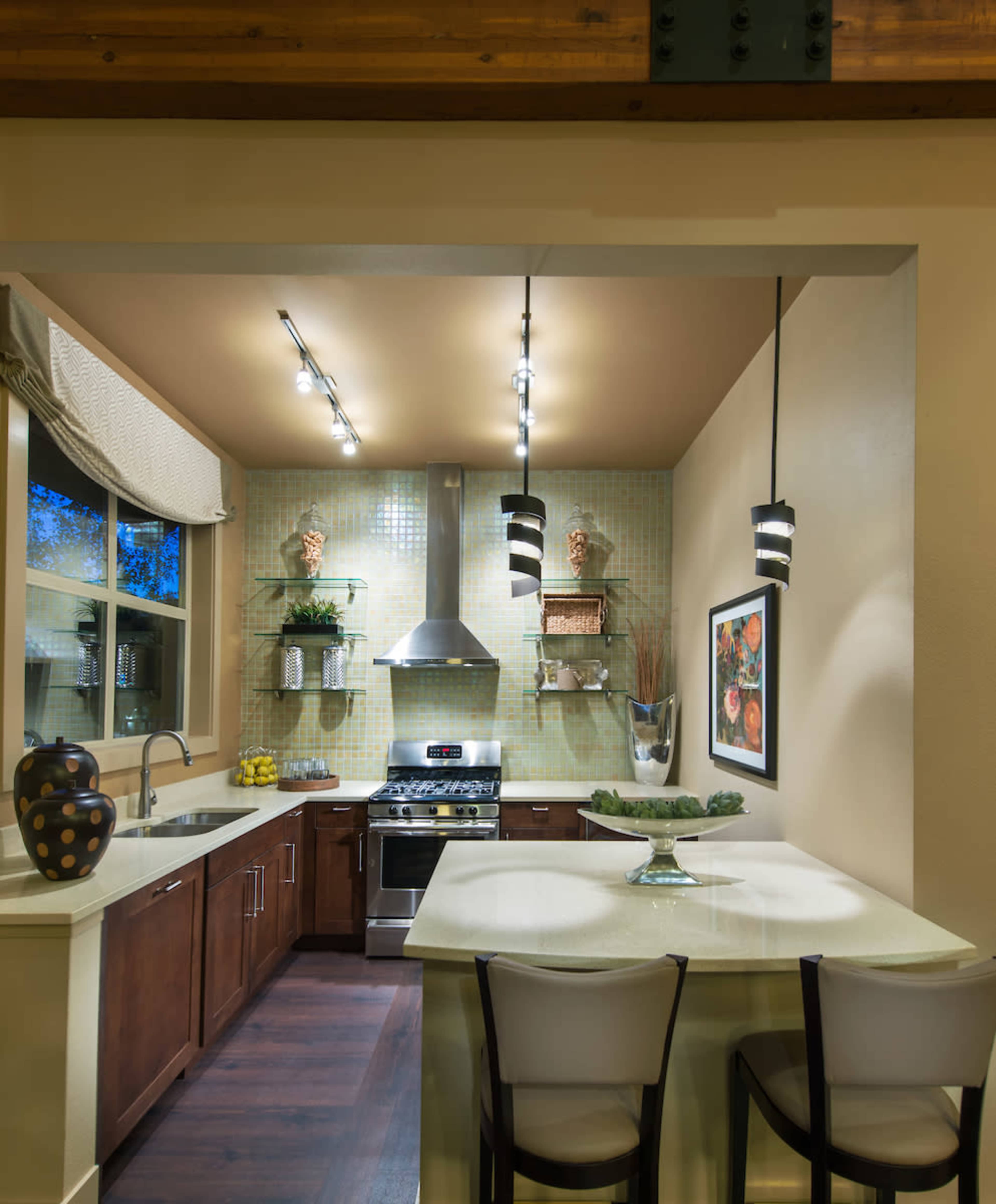 A modern kitchen with wooden cabinetry, a stainless steel stove, and a small dining area featuring two chairs and a counter with a decorative bowl.