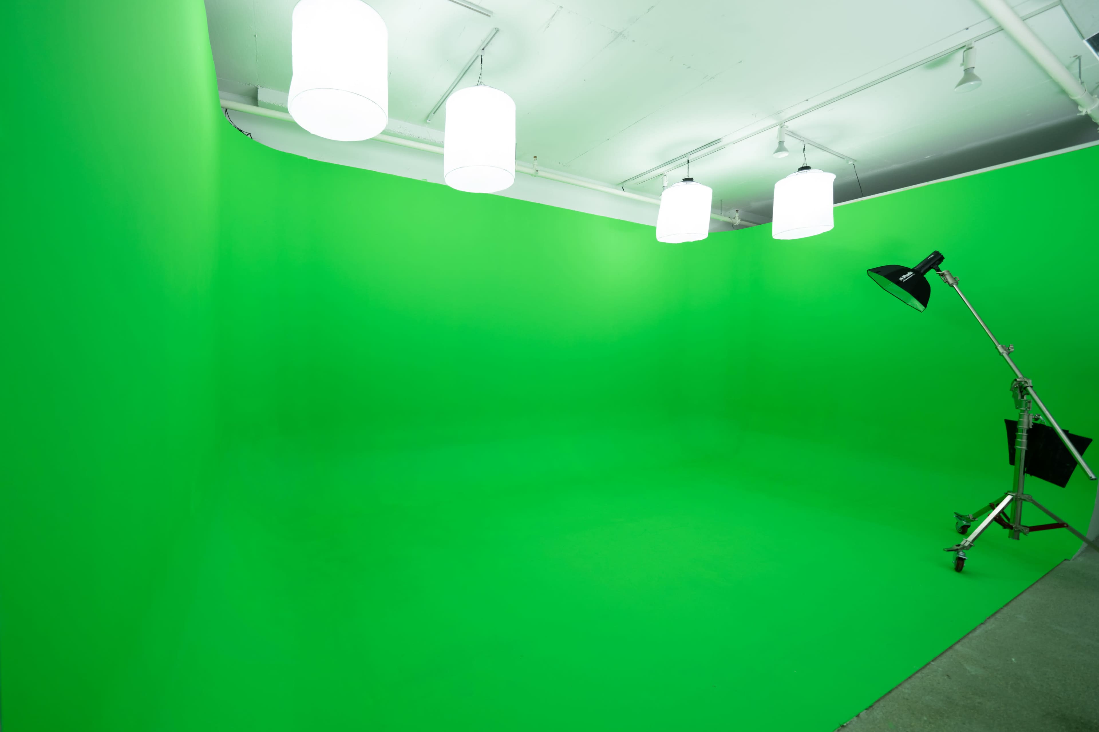 A green screen studio with four pendant lights and a standing lamp on the side.