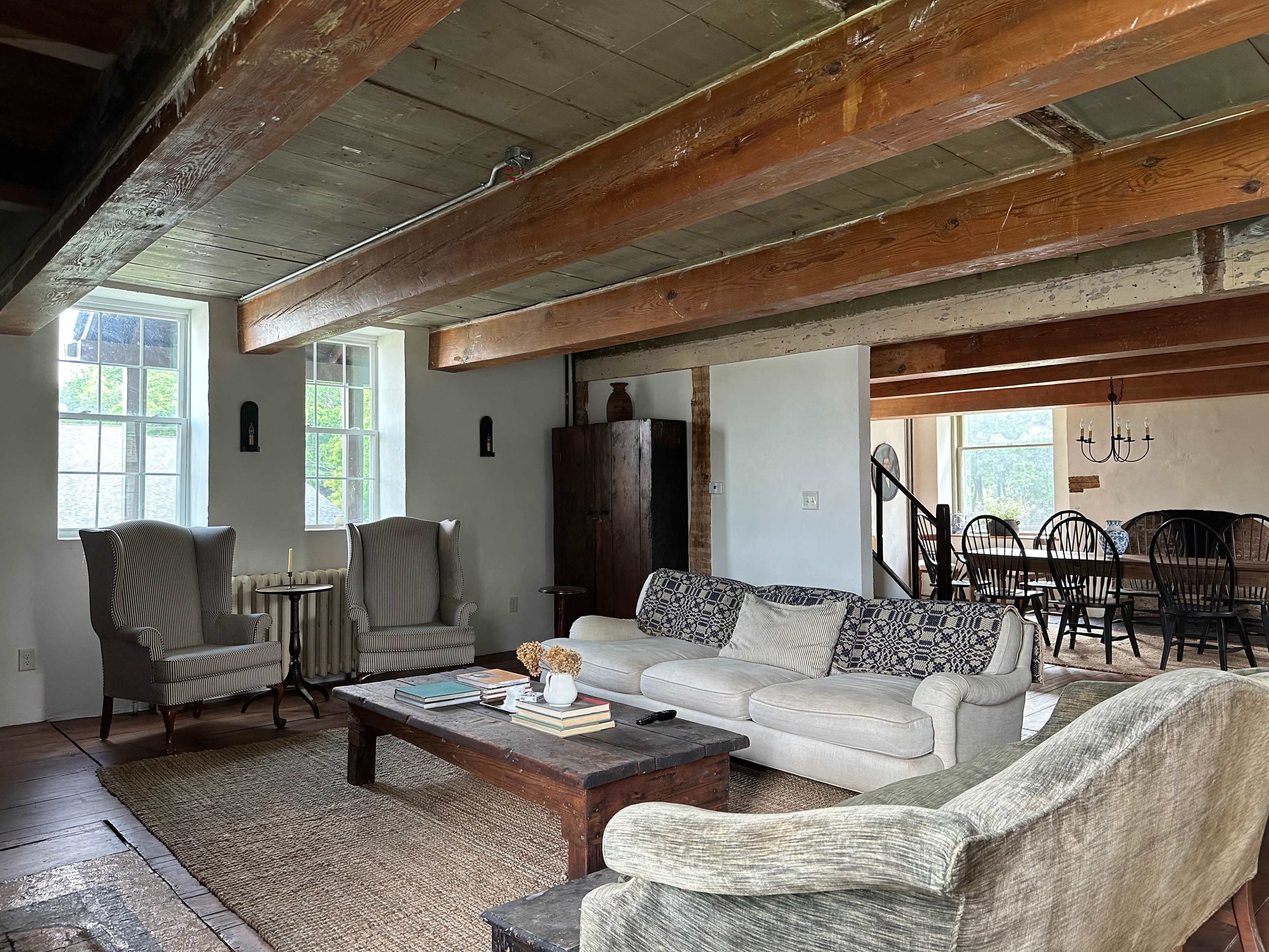 A spacious living area featuring two armchairs, a beige sofa, a wooden coffee table, and a dining area in the background with a large table and chairs.