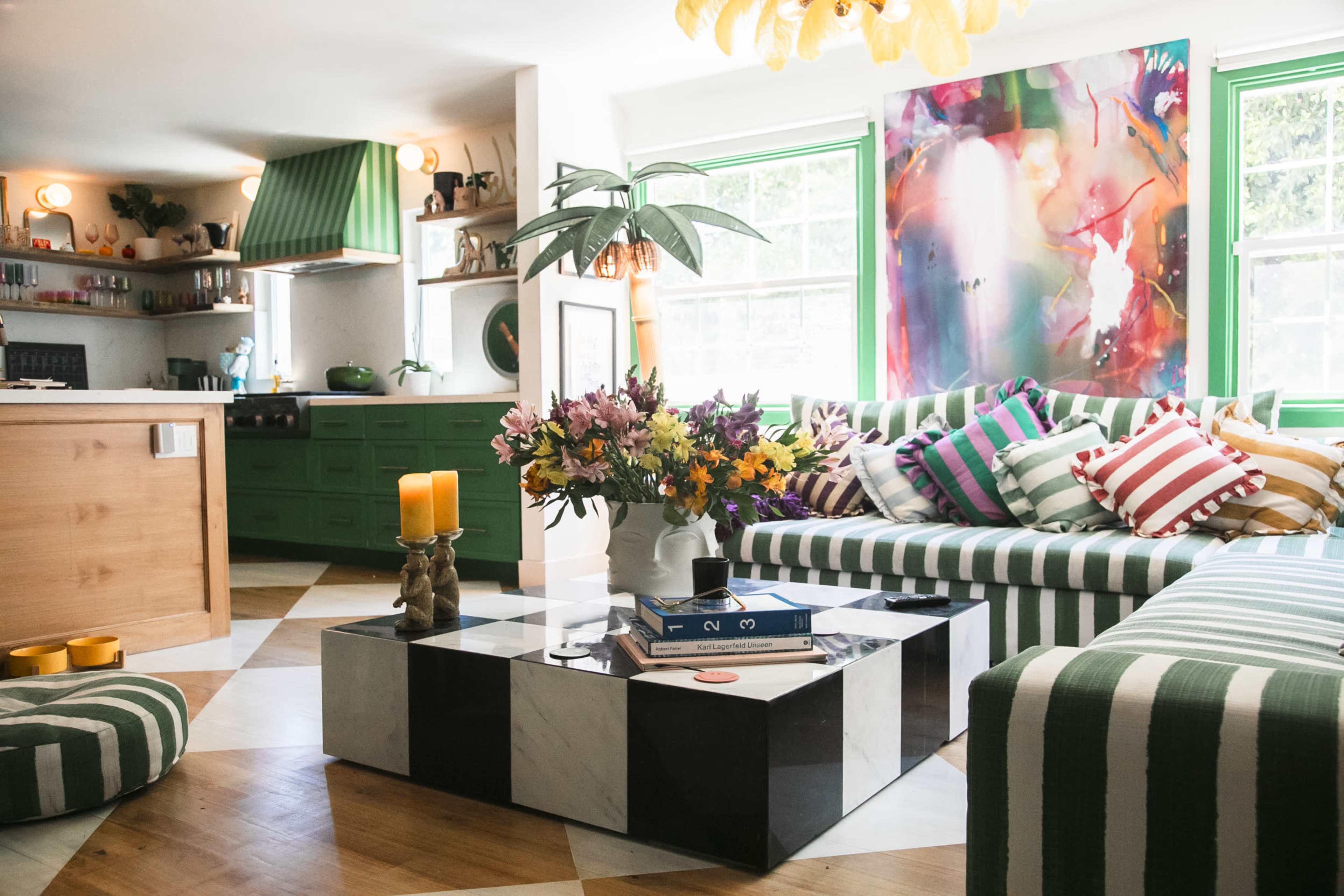 The living room features a striped green and white sofa, a marble coffee table, a vibrant abstract painting, and a kitchen with green cabinets.