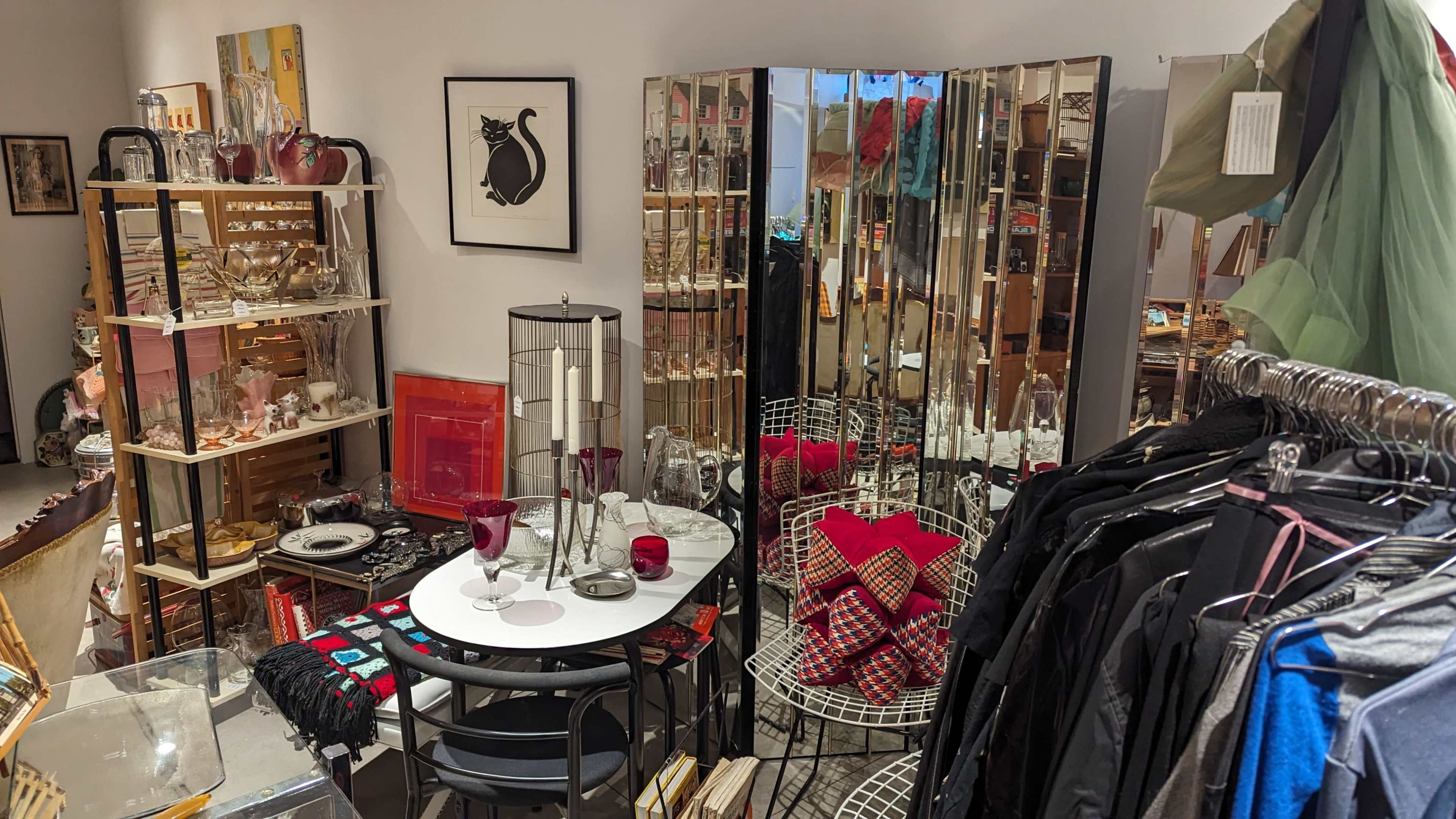 A cozy interior of a vintage shop, featuring a round table with decor items, mirrors, and a clothing rack.