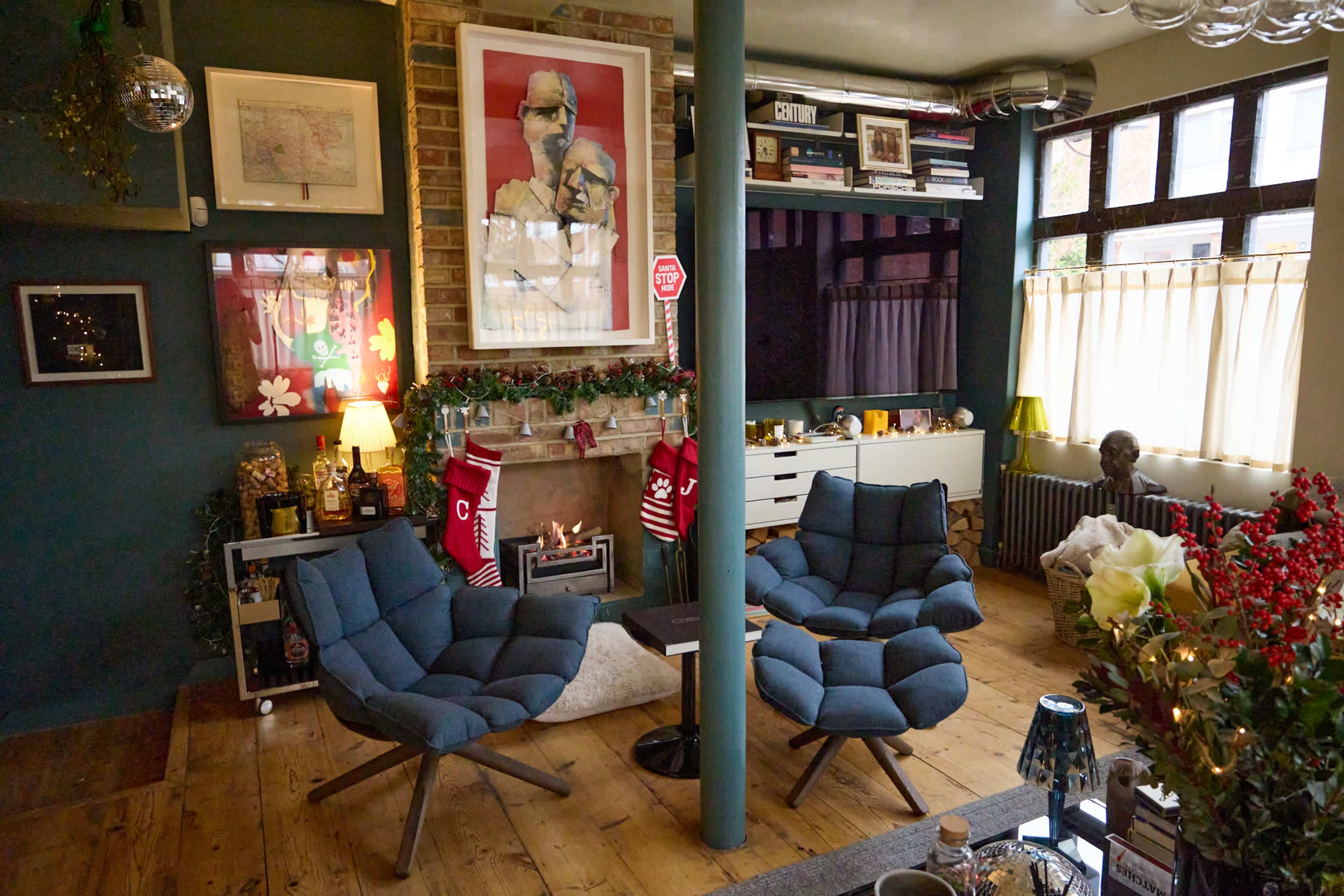 A cozy living room features two blue armchairs, a small fireplace, and shelves adorned with books and decor against a green wall.
