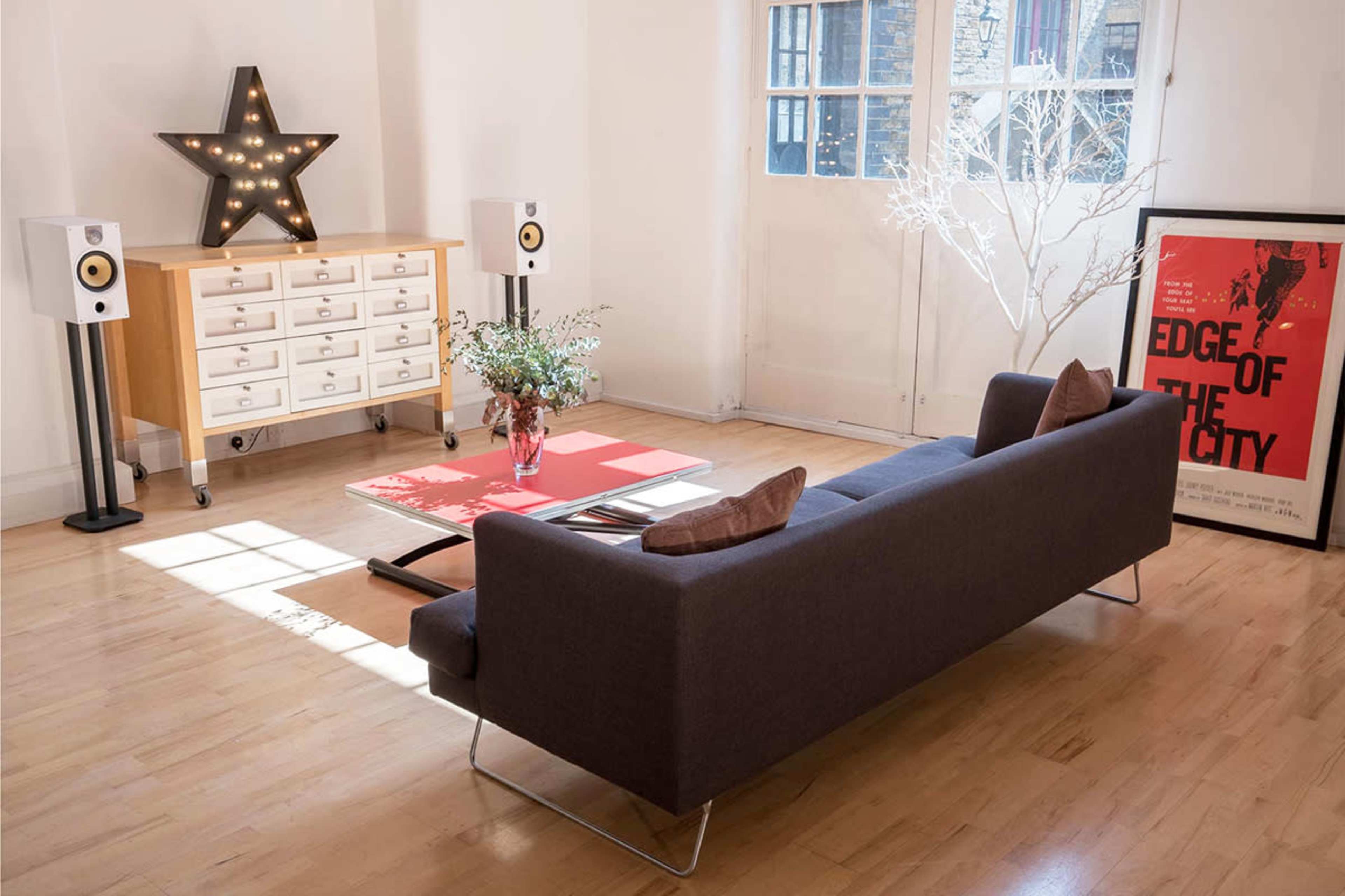 A modern living room featuring a grey sofa, a wooden dresser with decorative items, and a large movie poster framed on the floor.