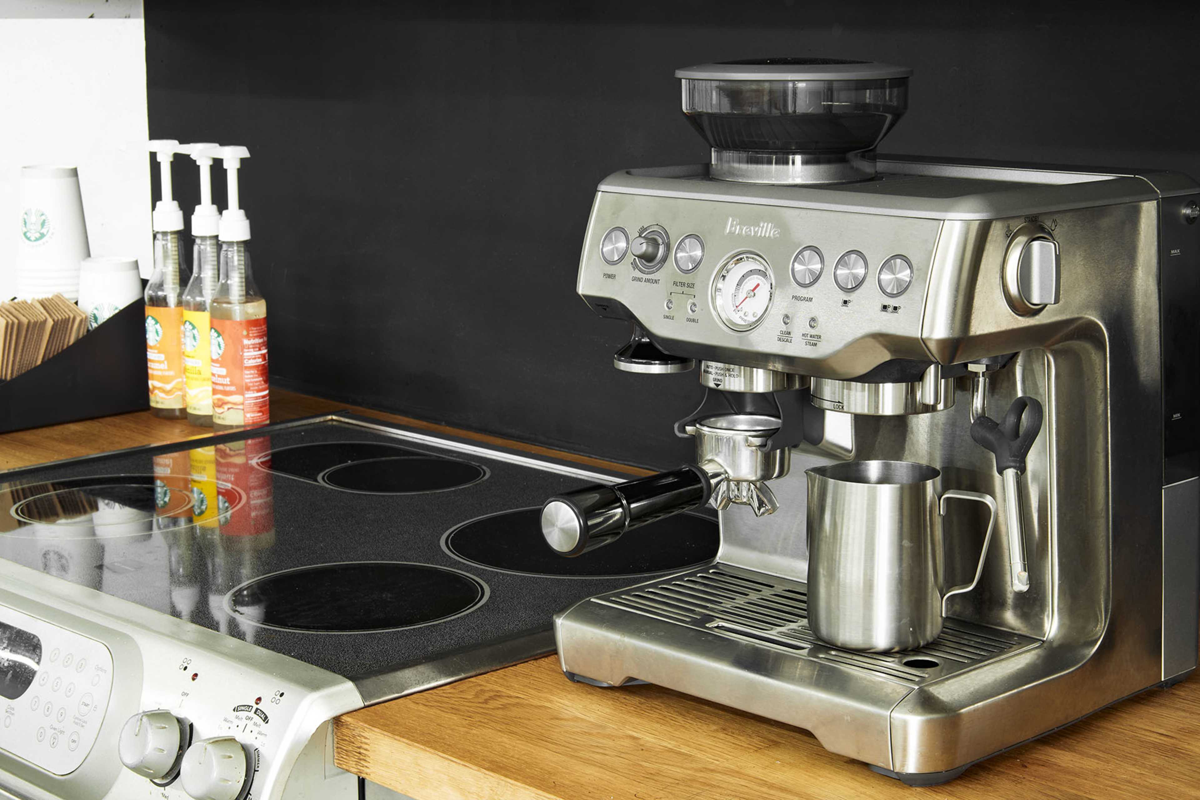 A stainless steel espresso machine is positioned on a wooden countertop beside a smooth cooktop.