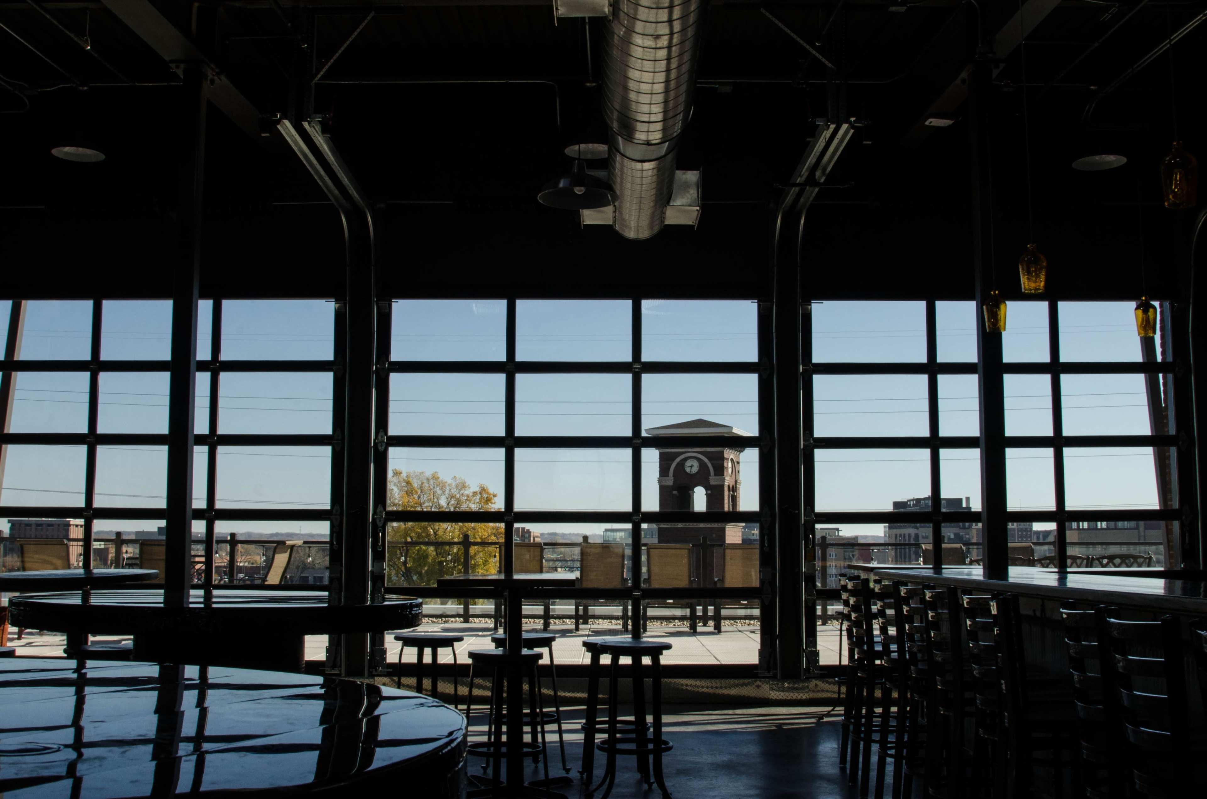 A modern interior with tall windows reveals a view of a clock tower and outdoor seating area.