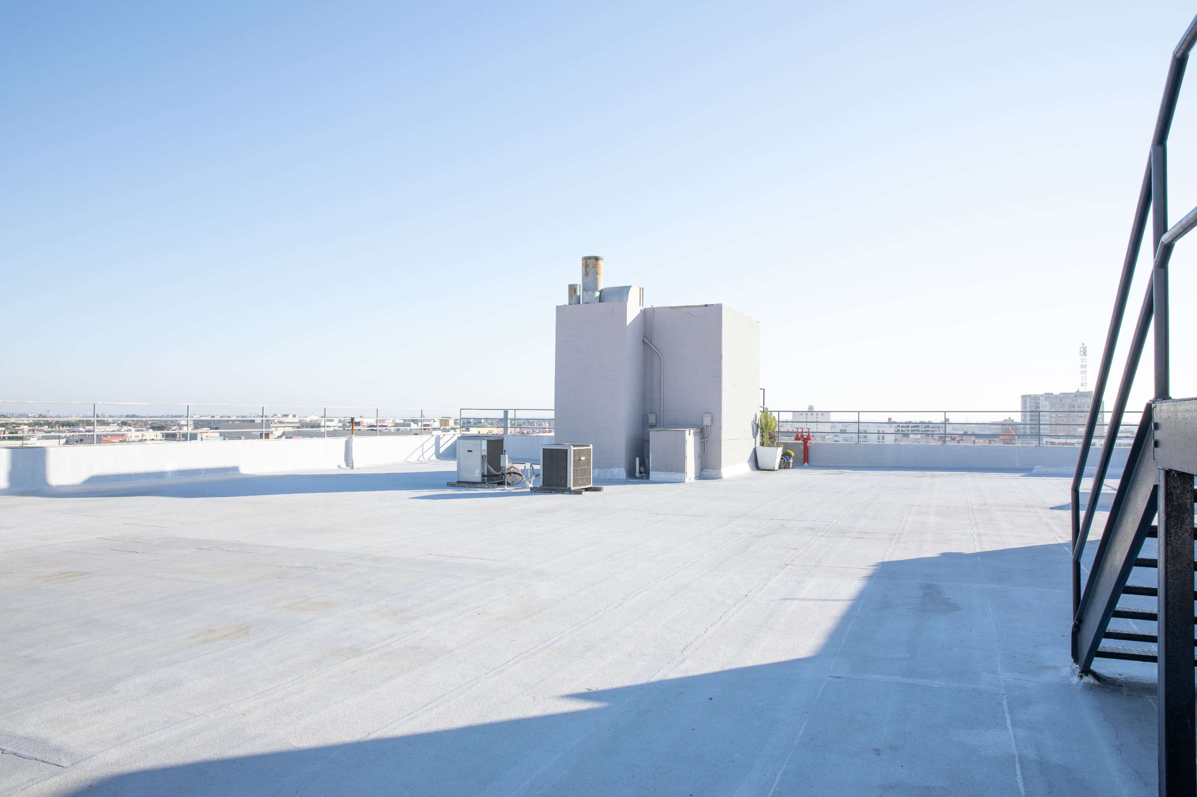 The image shows a flat rooftop with HVAC units and a tall structure against a clear blue sky.