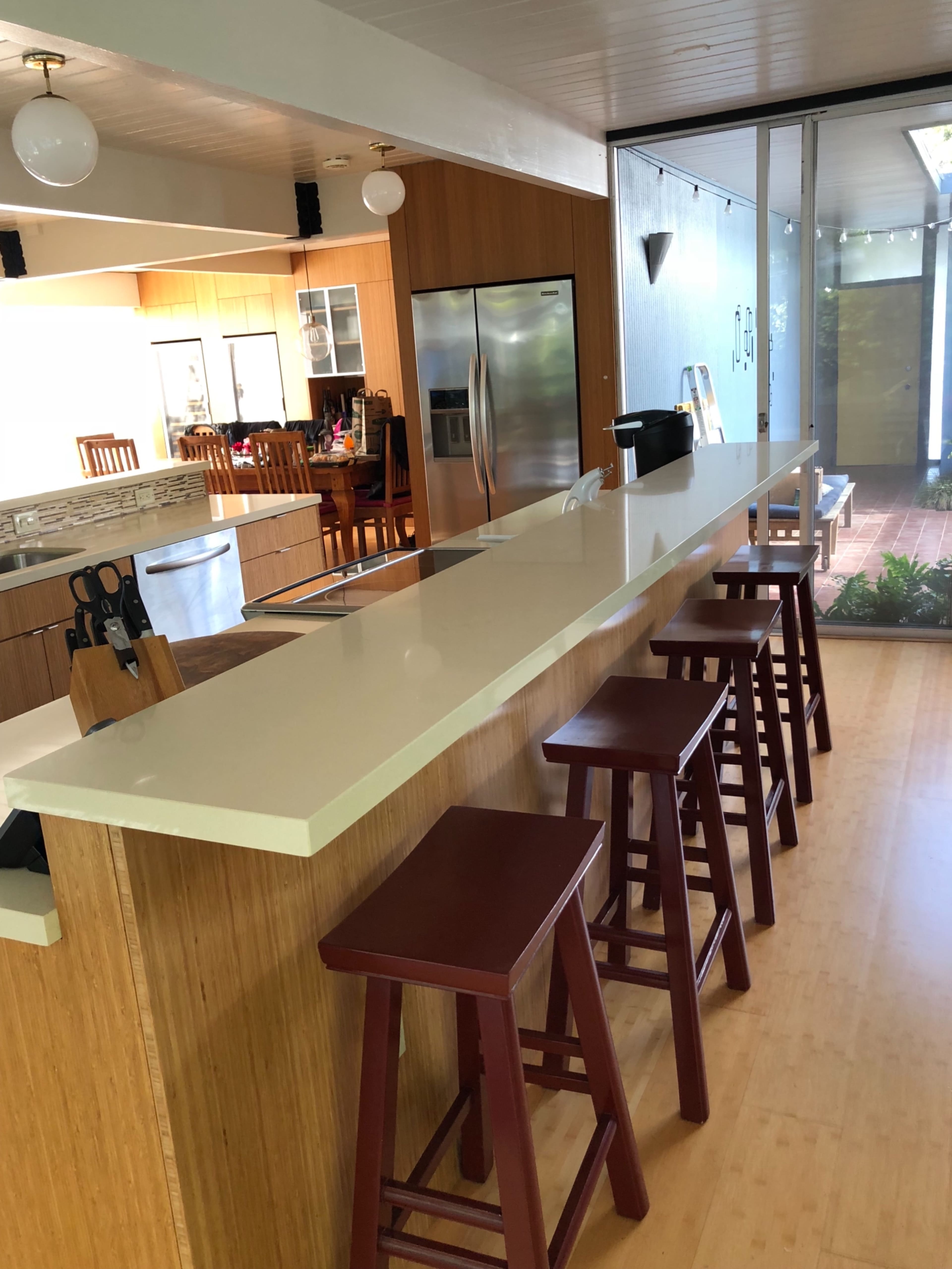 A modern kitchen with a long, white countertop and four maroon stools positioned along one side.