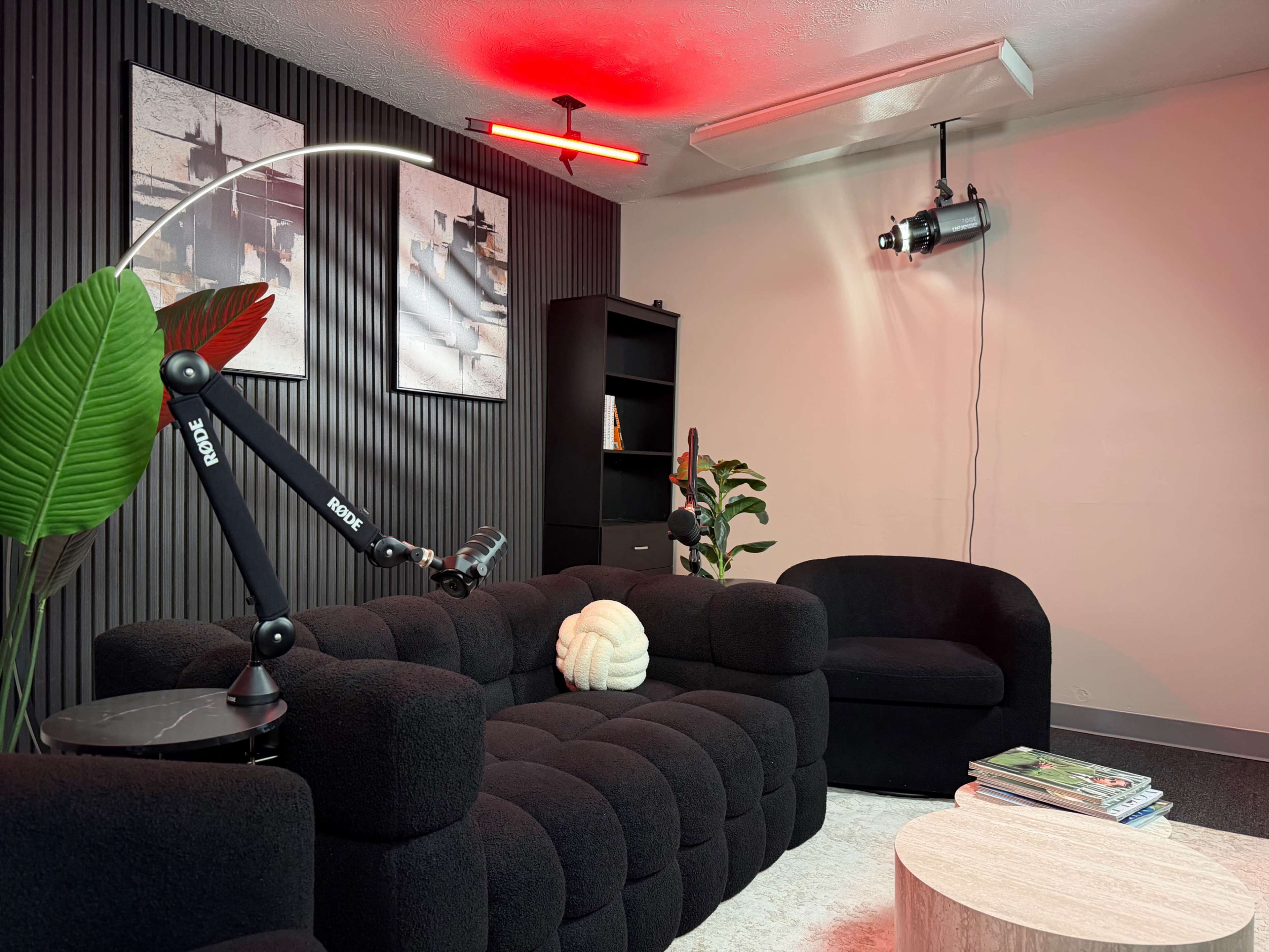 The image shows a modern lounge area featuring a dark-colored sofa, a small round coffee table, decorative plants, and artwork on the walls, illuminated by red lighting.