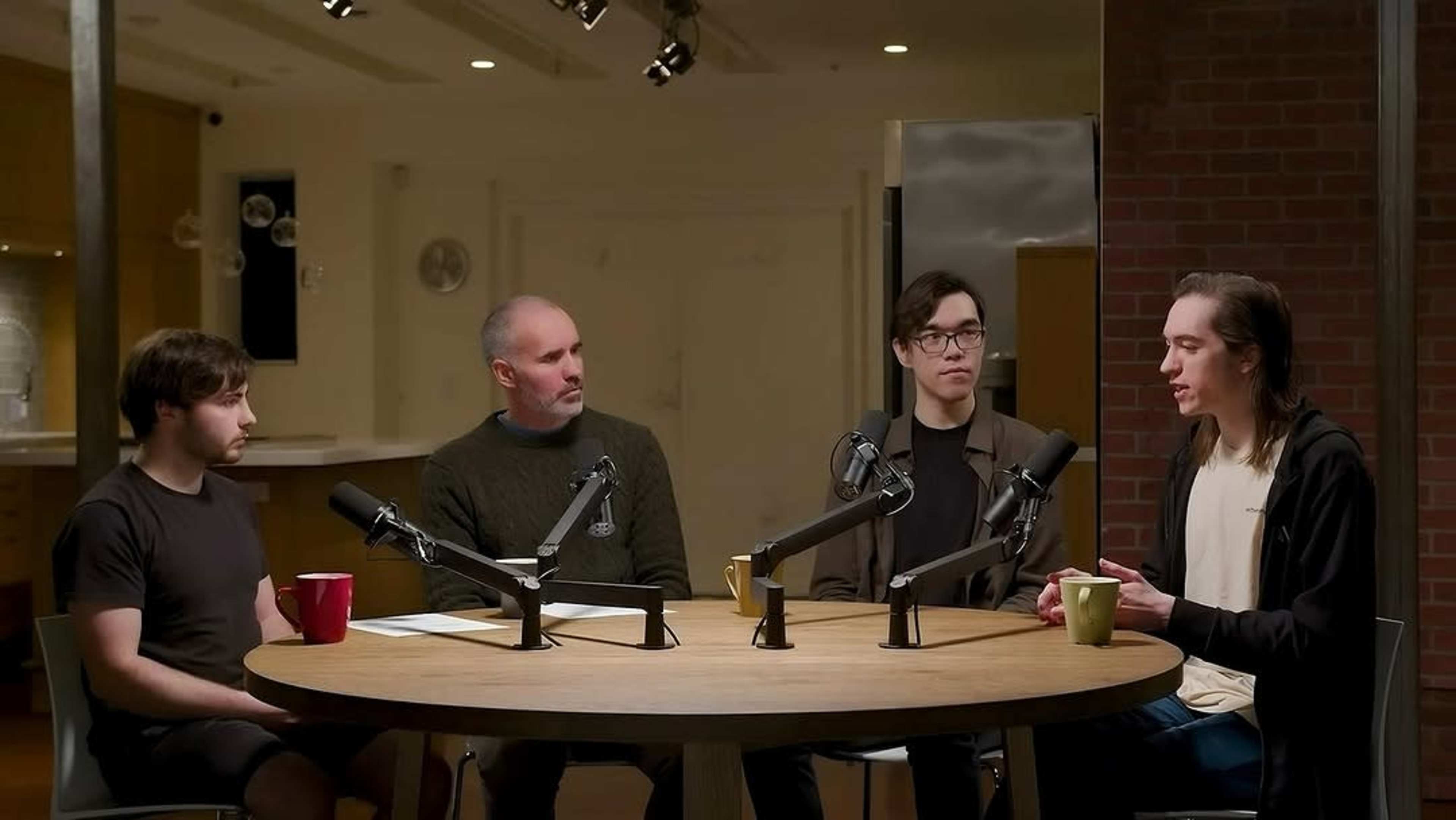 Four people are seated around a round table equipped with microphones in a well-lit room.