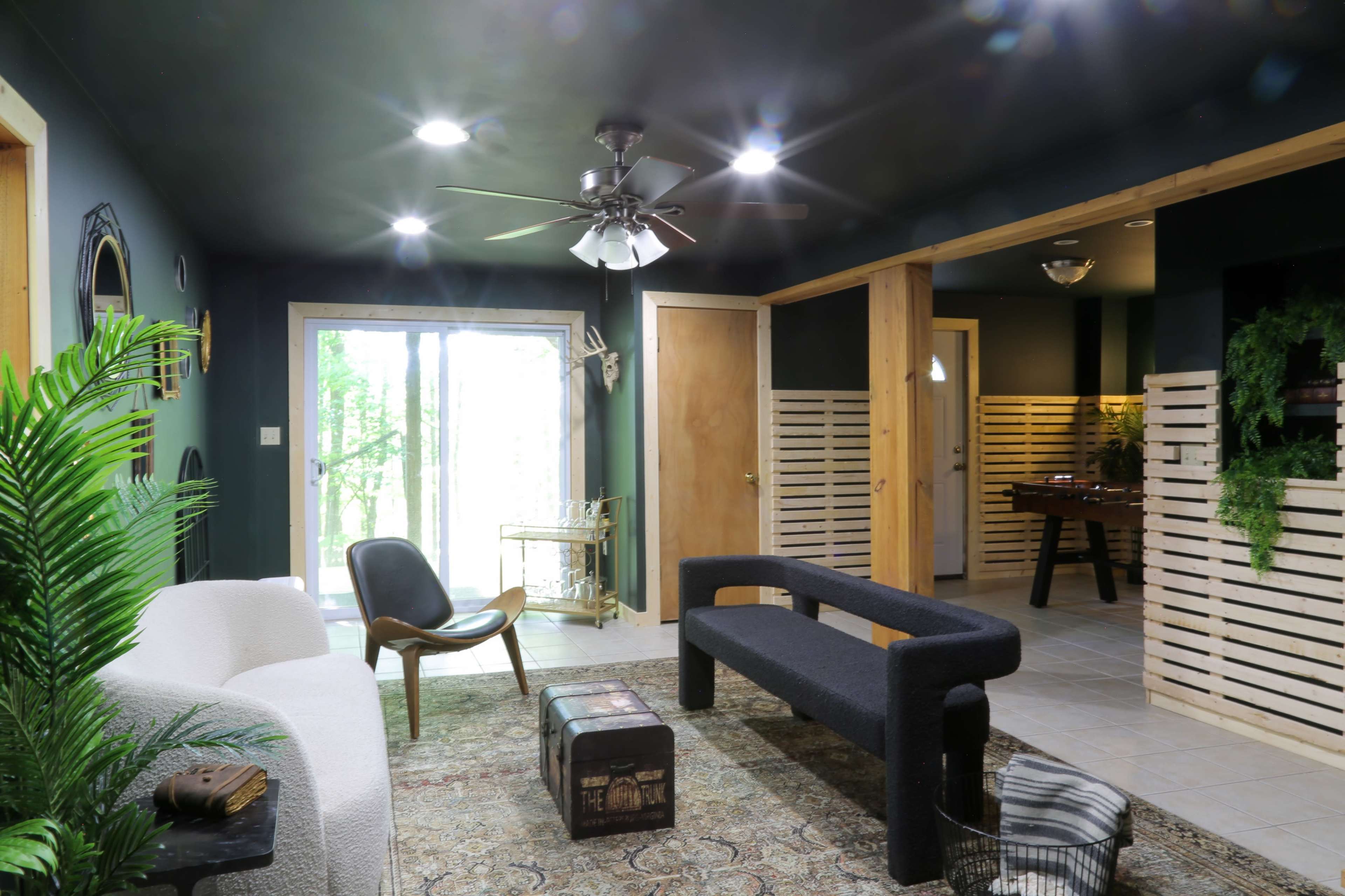 A modern living space features a white sofa, a black bench, and a wooden accent wall, with large windows leading to an outdoor area.