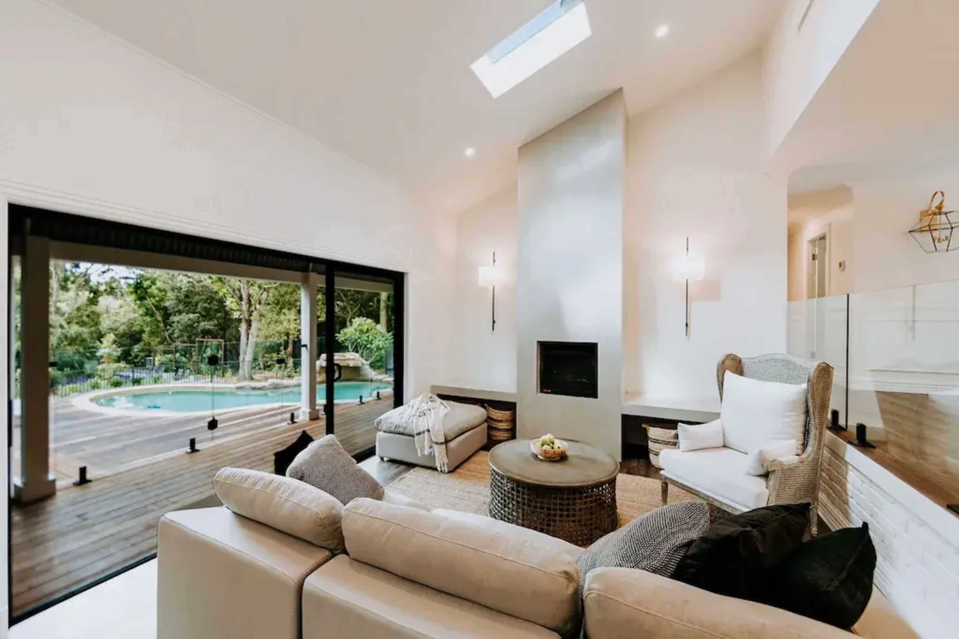 A modern living room features a fireplace, large windows overlooking a pool area, and comfortable seating arrangements.