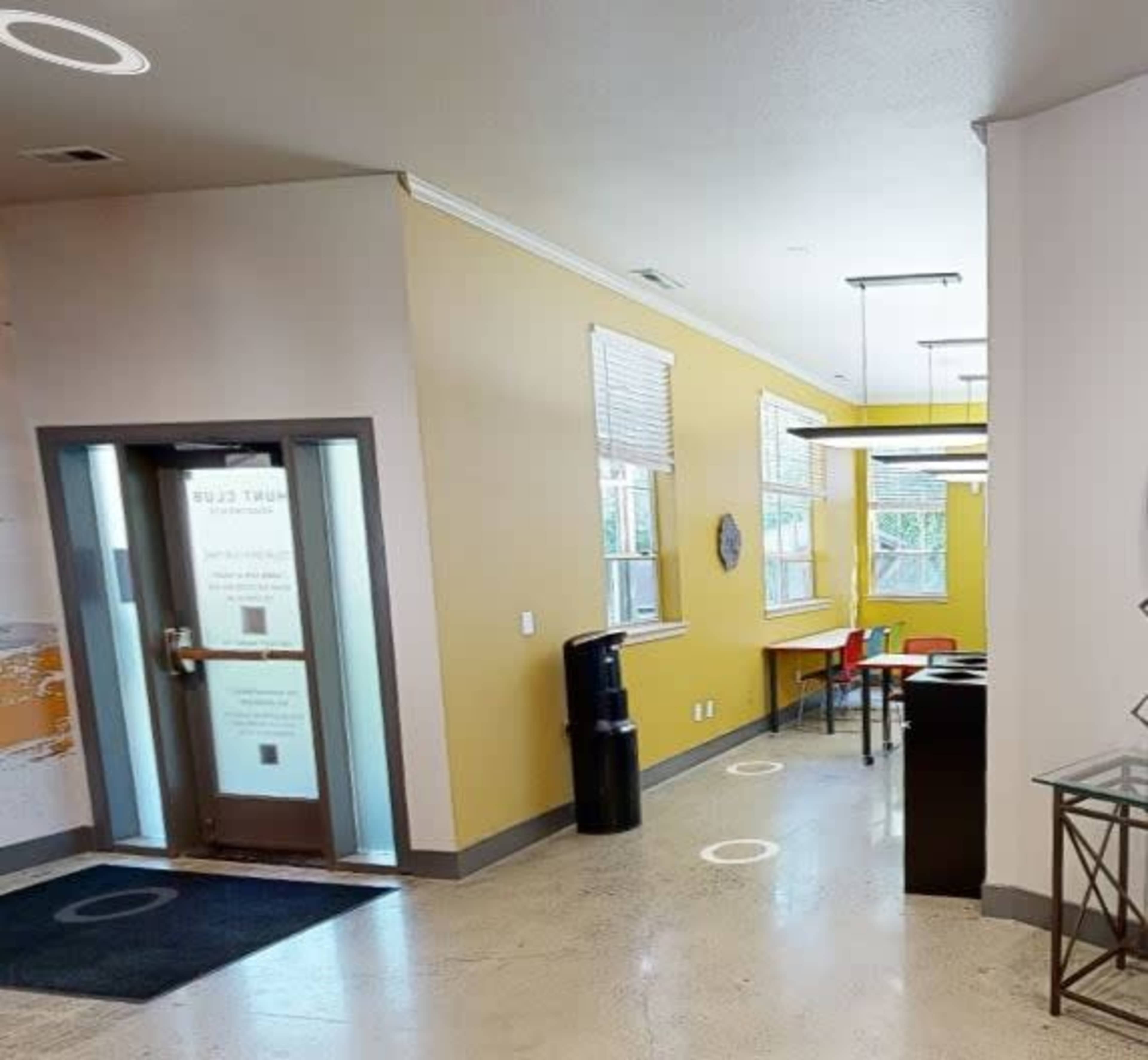 An interior space featuring a yellow wall, a door leading outside, a water cooler, and a few tables and chairs arranged for seating.