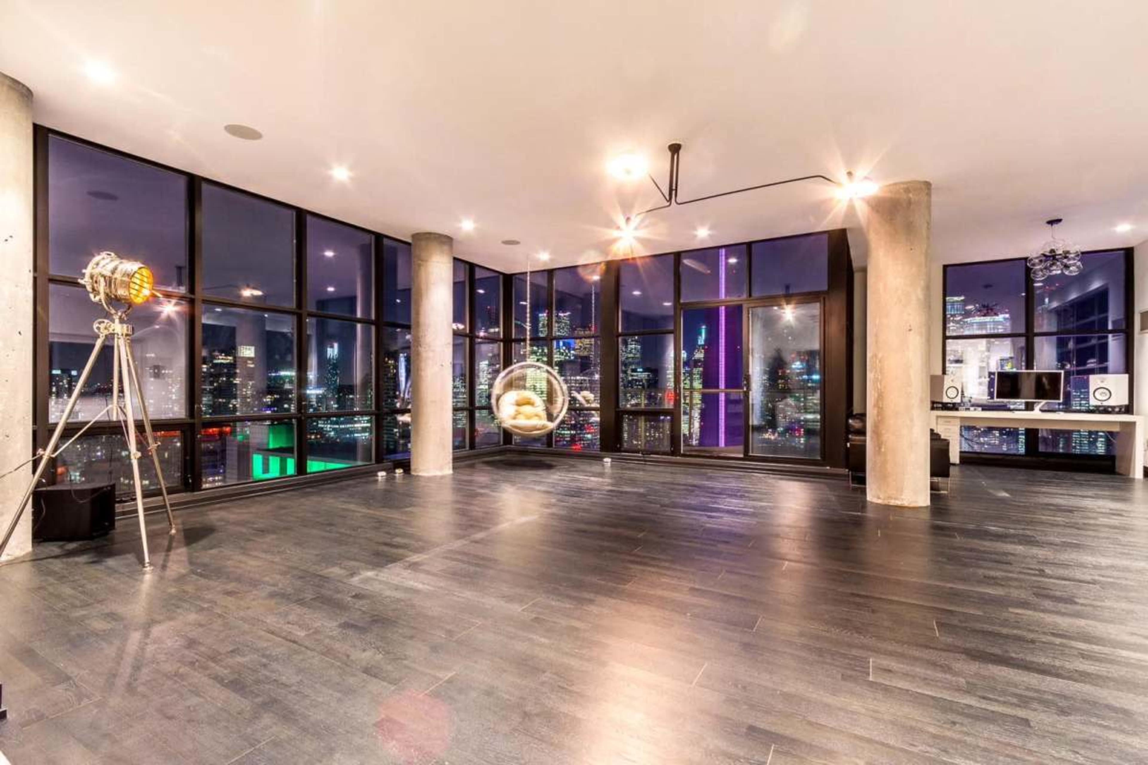 The image shows a spacious modern interior with large windows overlooking a city skyline at night, featuring concrete pillars and sleek flooring.