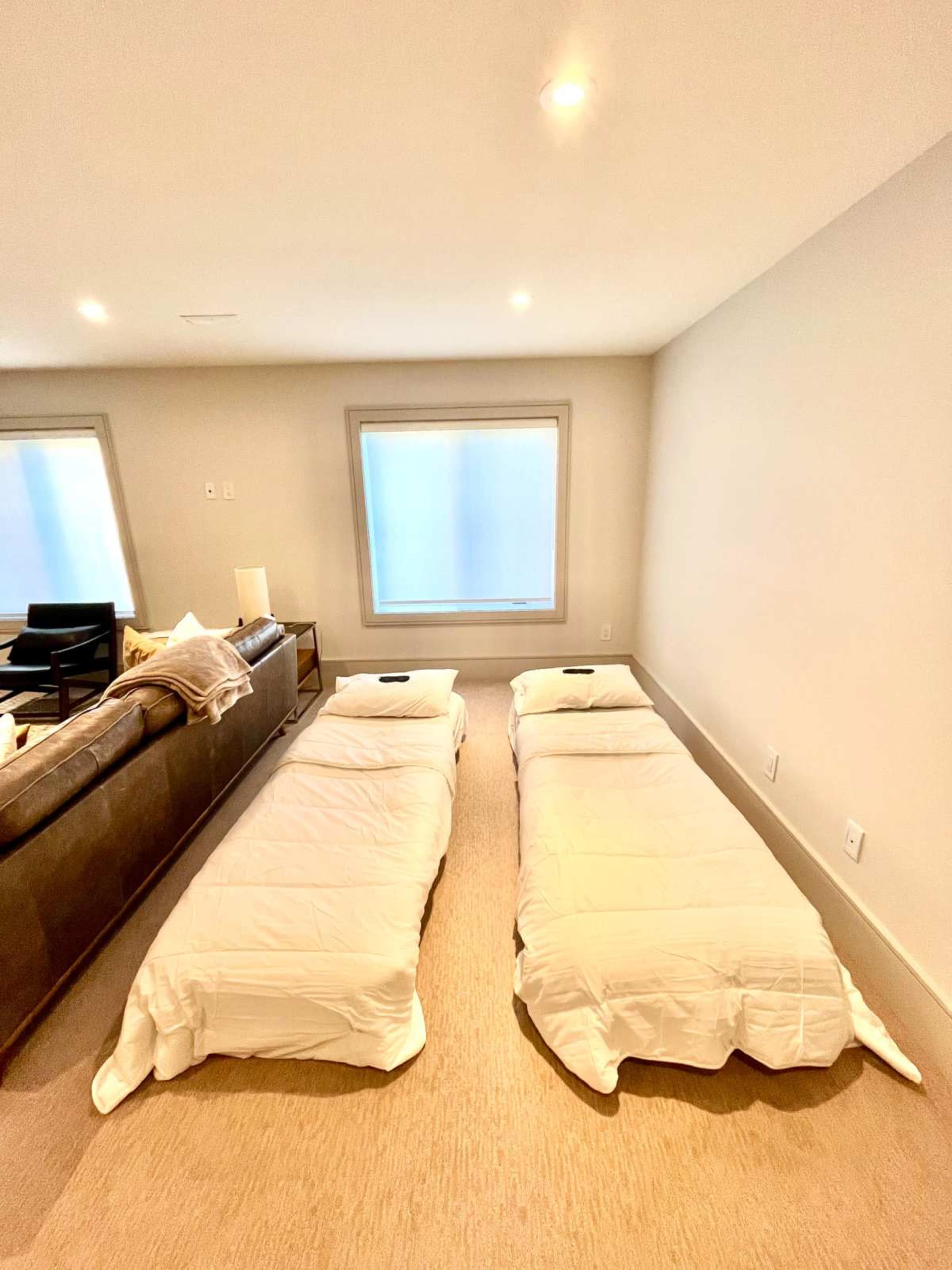 The image shows two single beds made with white bedding placed parallel to each other on a carpeted floor in a well-lit room.