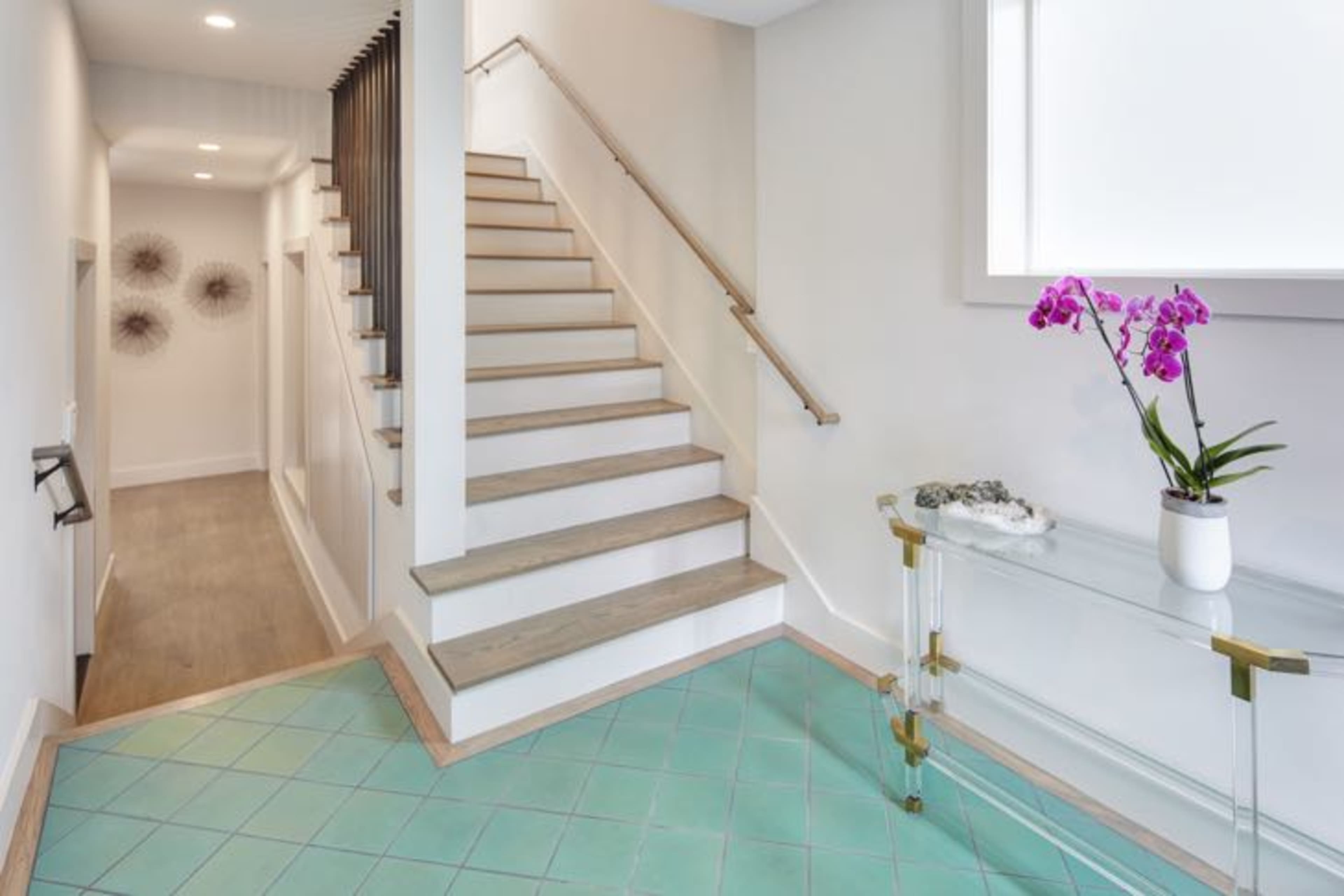 A modern entryway features a staircase with light wood steps and a glass console table adorned with a purple orchid.