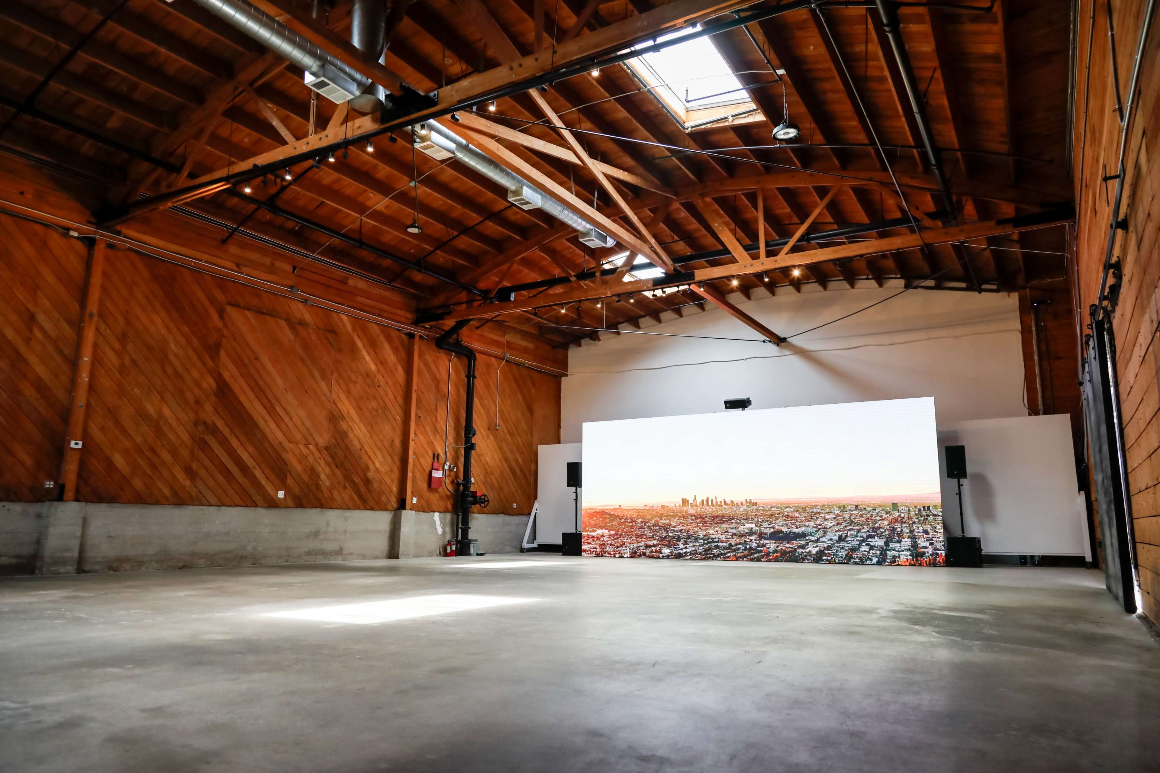 A spacious room with wooden beams features a large video screen displaying a city skyline.