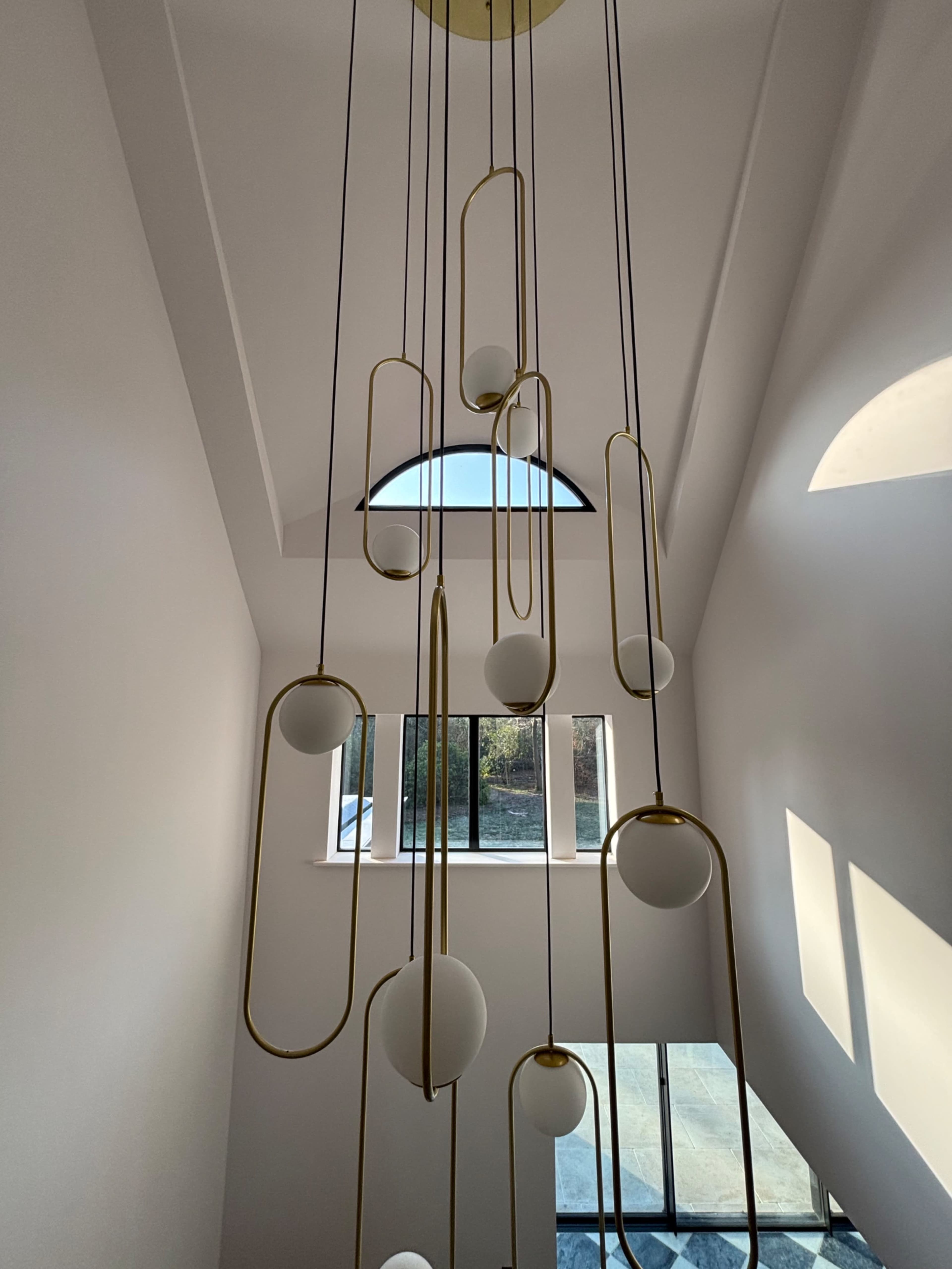 The image depicts a modern stairwell featuring a series of pendant lights suspended from the ceiling, with a large window providing natural light.