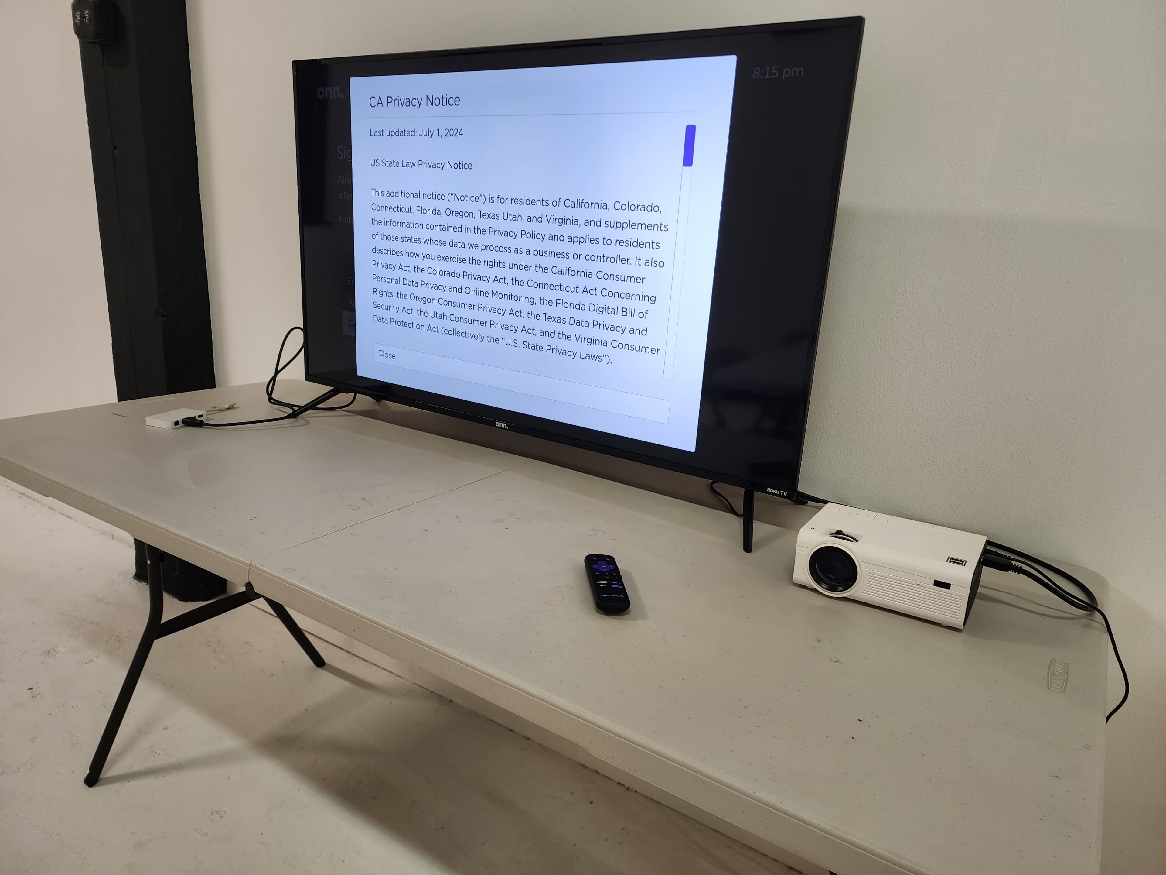 A television displays a California Privacy Notice on a table, alongside a remote control and a projector.
