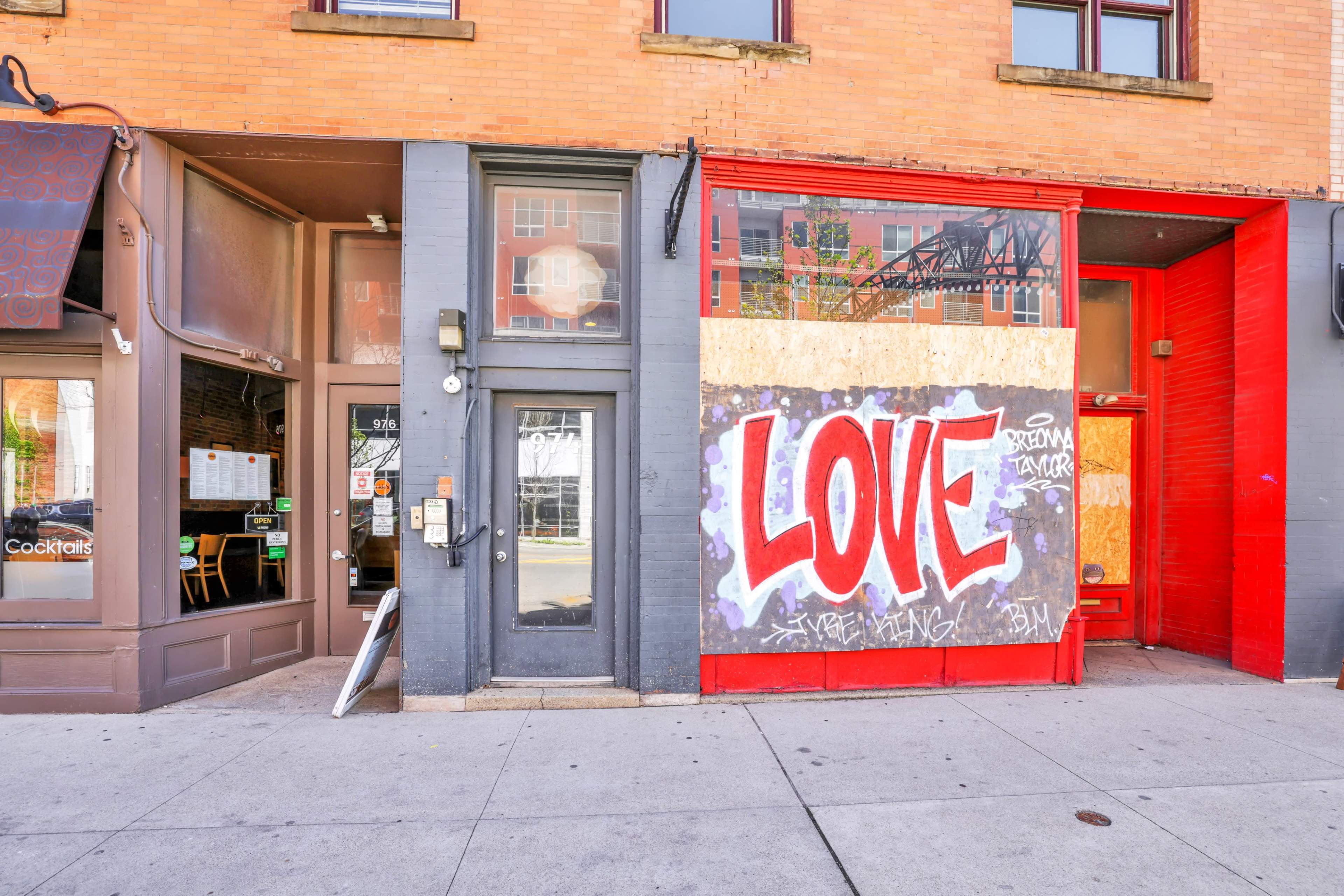 A storefront with a vibrant "LOVE" mural on a boarded-up window, next to a business with visible outdoor seating.