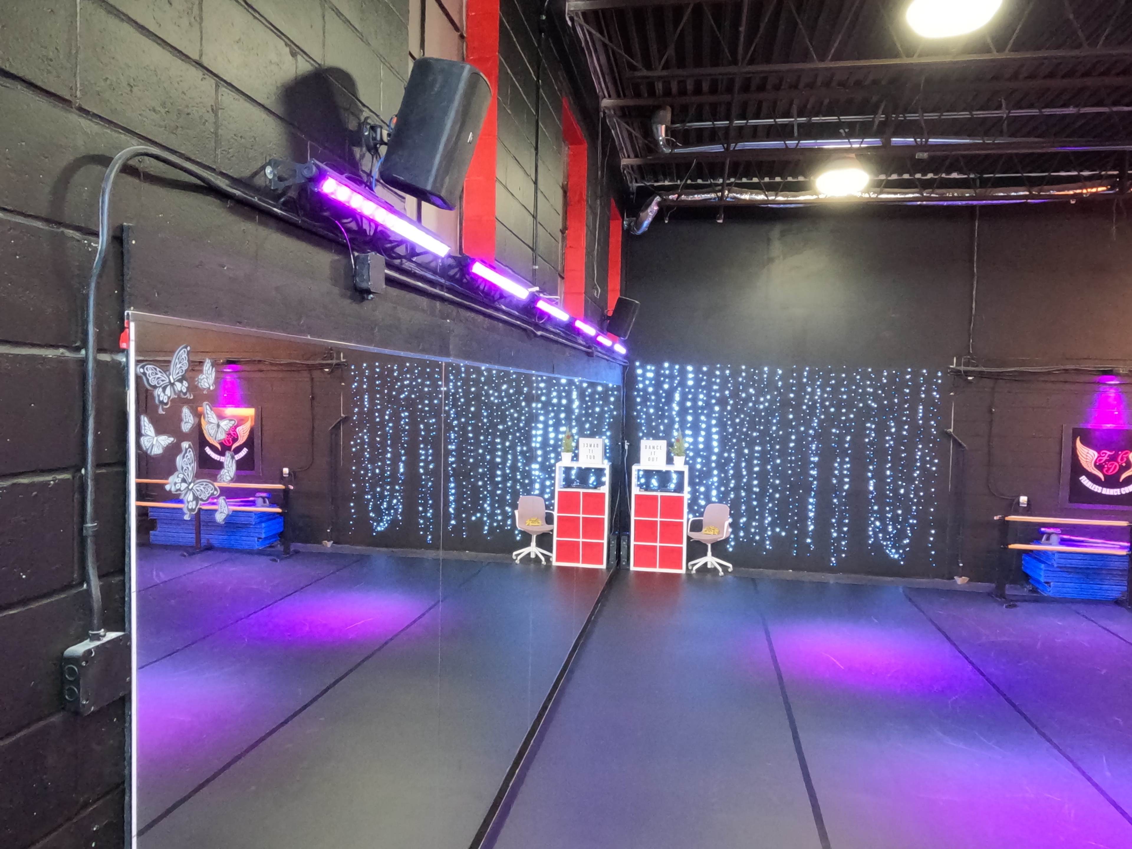 The image shows a dance studio with mirrors, bright lighting, and a backdrop of sparkling lights on one wall.