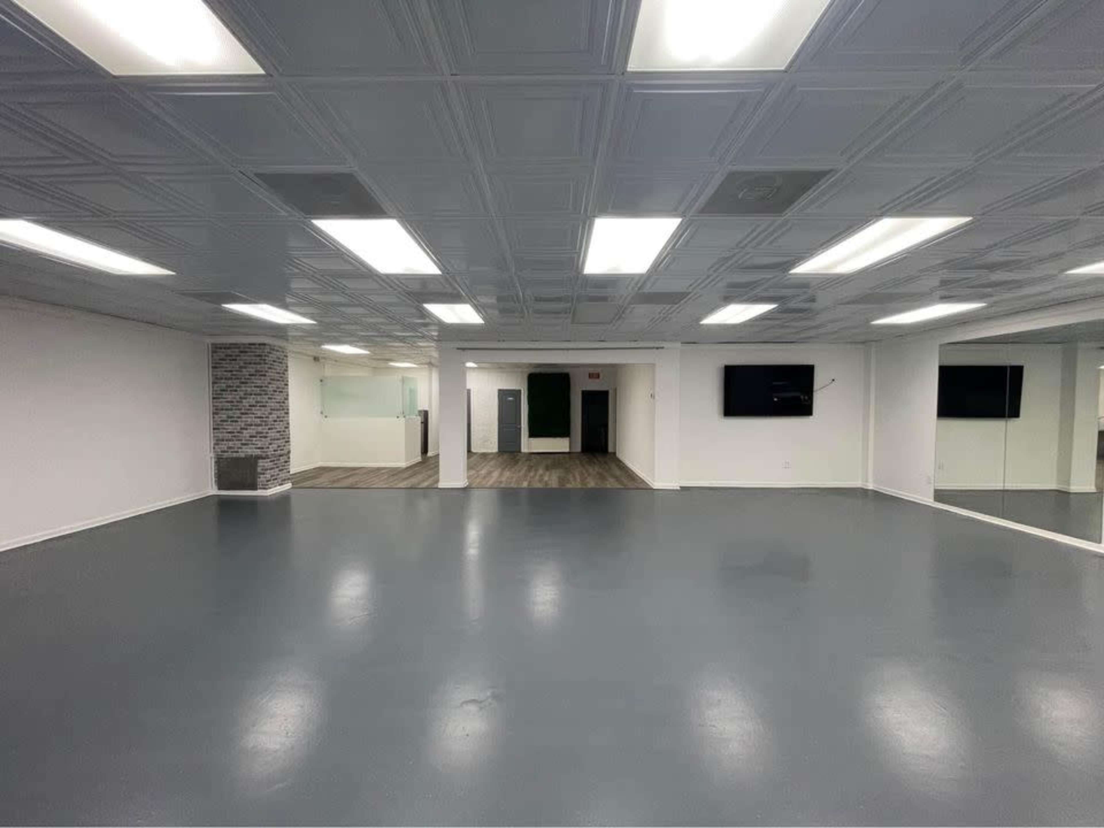 The image shows a spacious, well-lit room with a smooth gray floor and a mirrored wall, featuring a reception area in the background.
