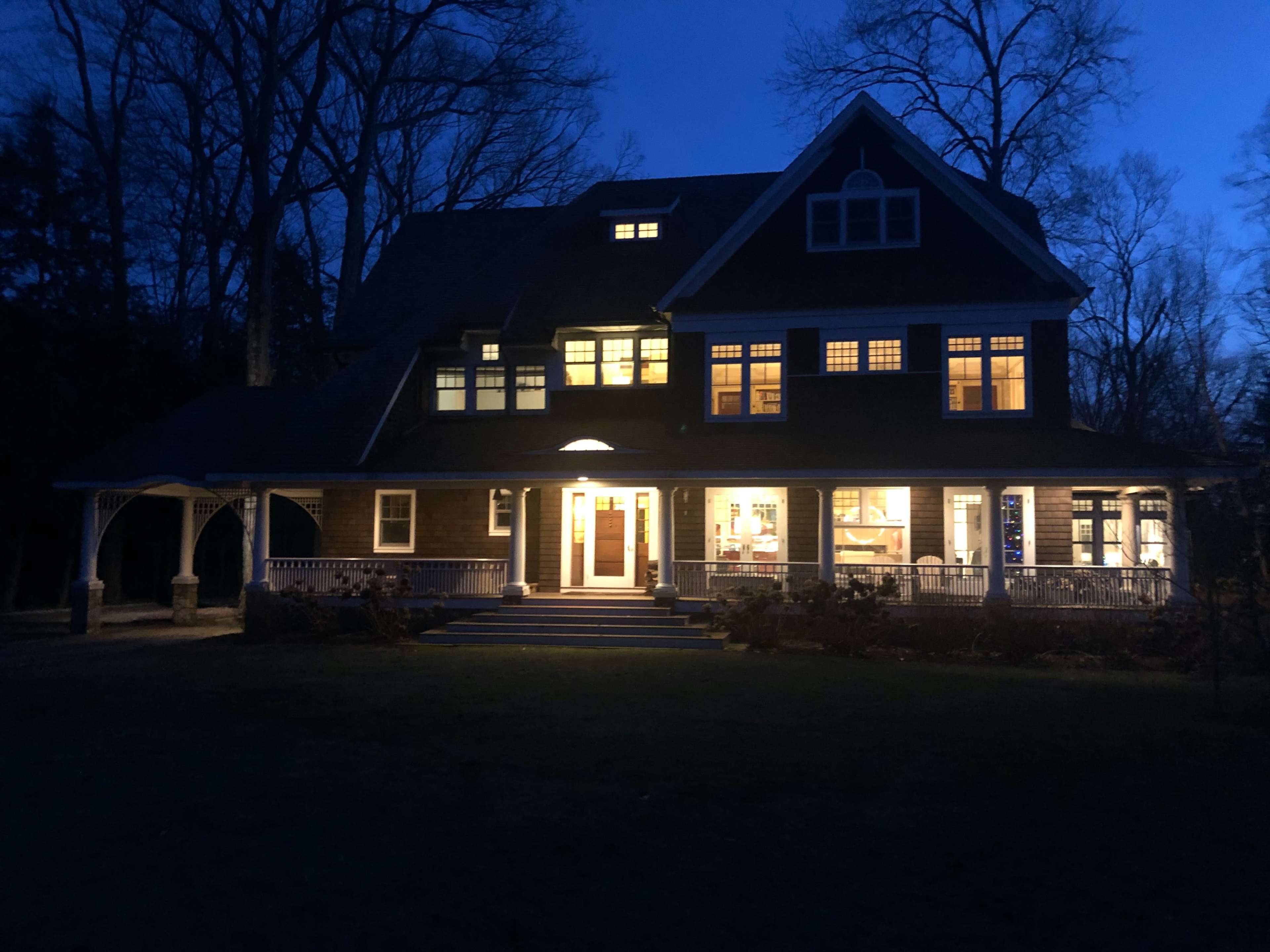 A large, illuminated house stands at dusk, showcasing multiple windows and a welcoming entrance.