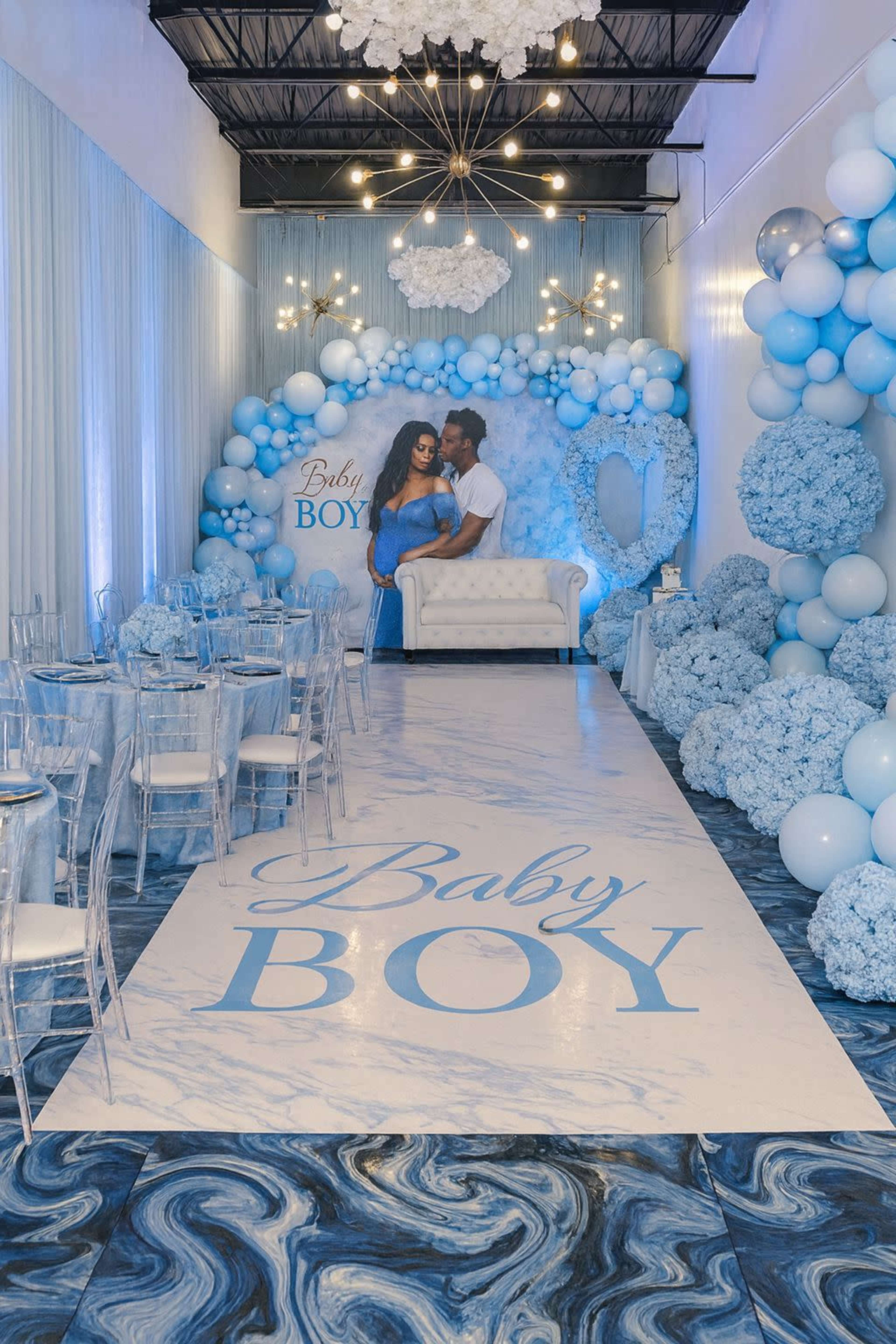 A couple poses in an elegantly decorated event space featuring blue-themed decorations for a baby boy celebration.