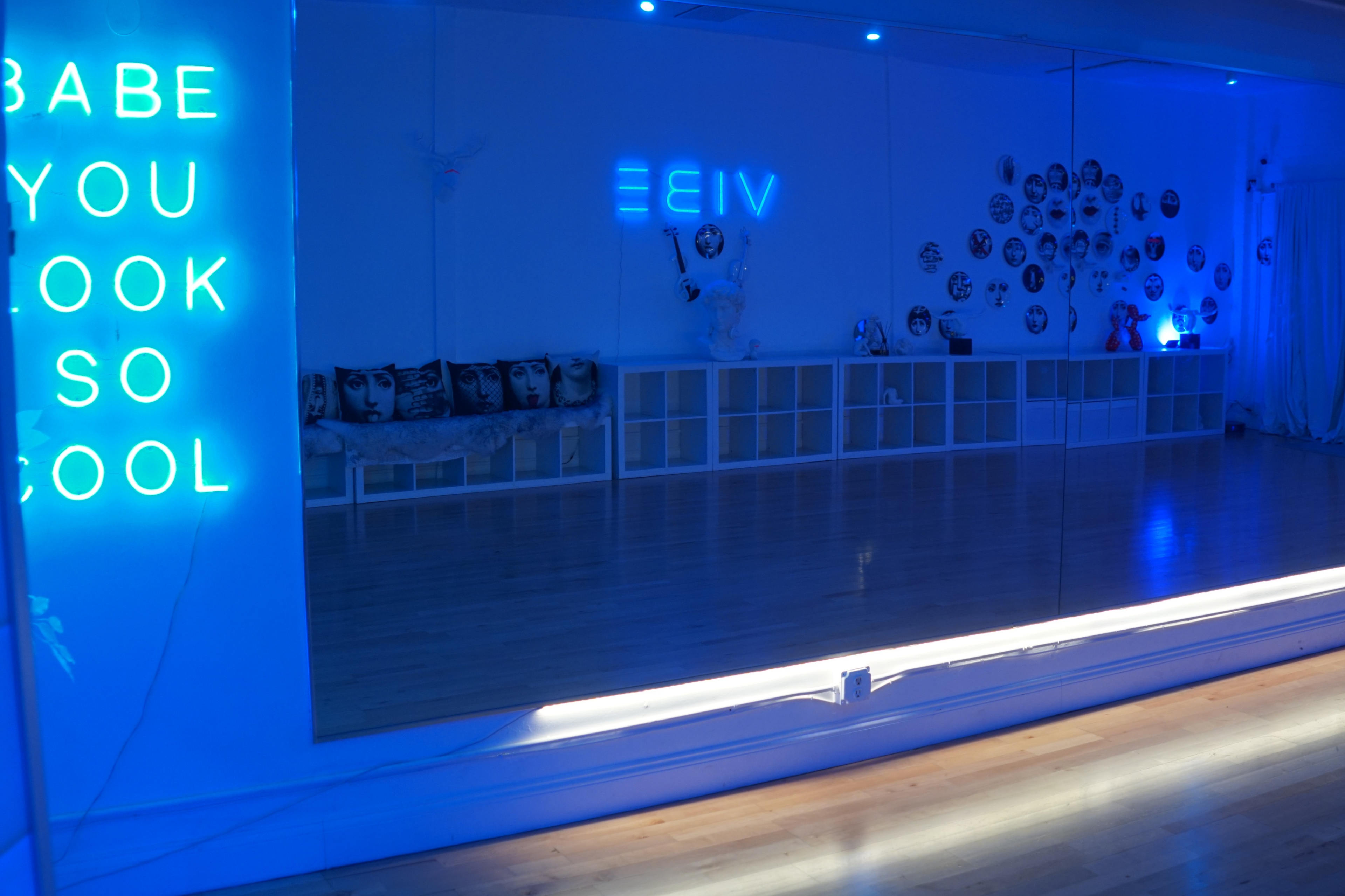 A modern dance studio with blue lighting, a large mirror, and a wall decorated with black-and-white portraits.