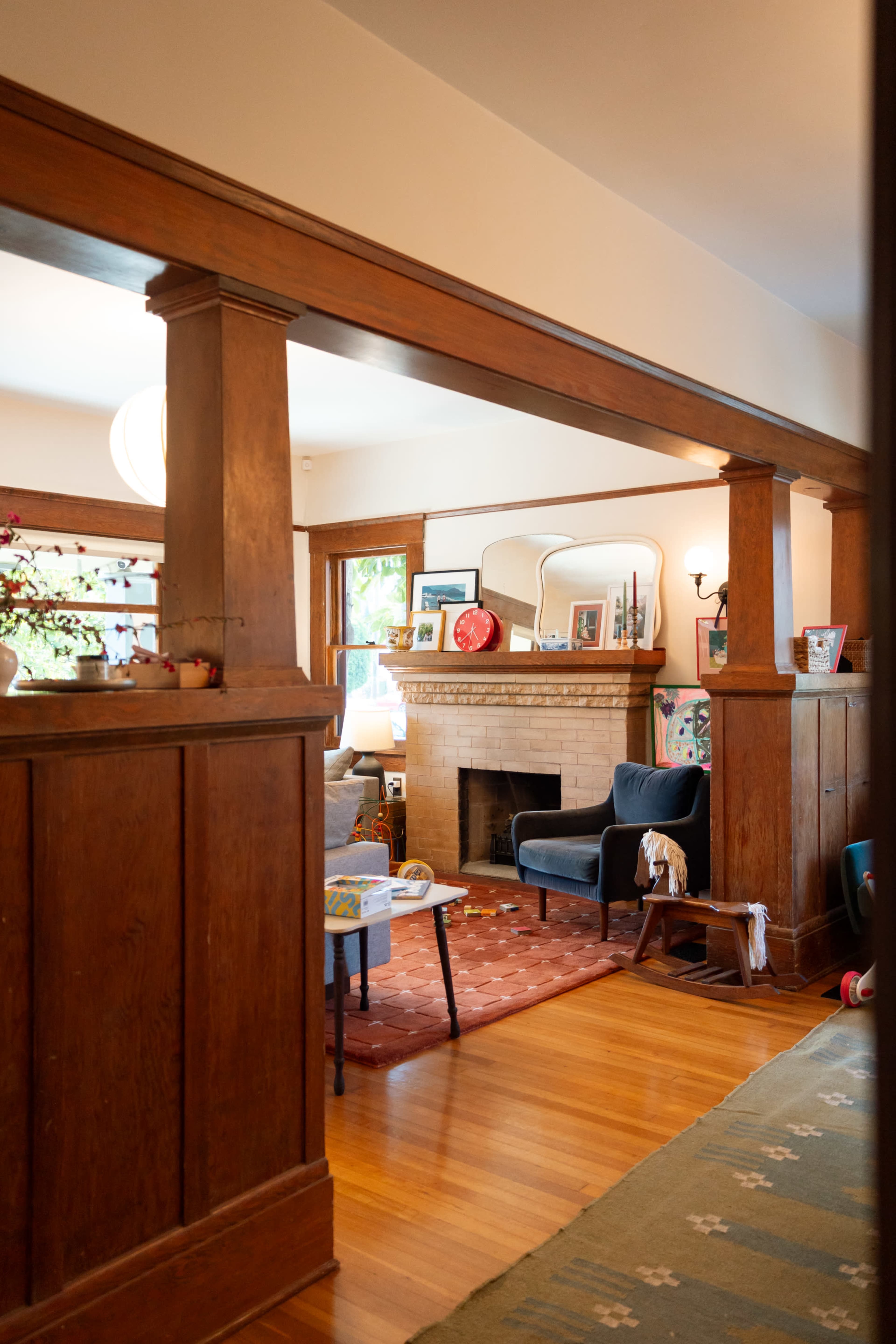 The image shows a cozy living room with wooden beams, a fireplace, and a black armchair, framed by a doorway.
