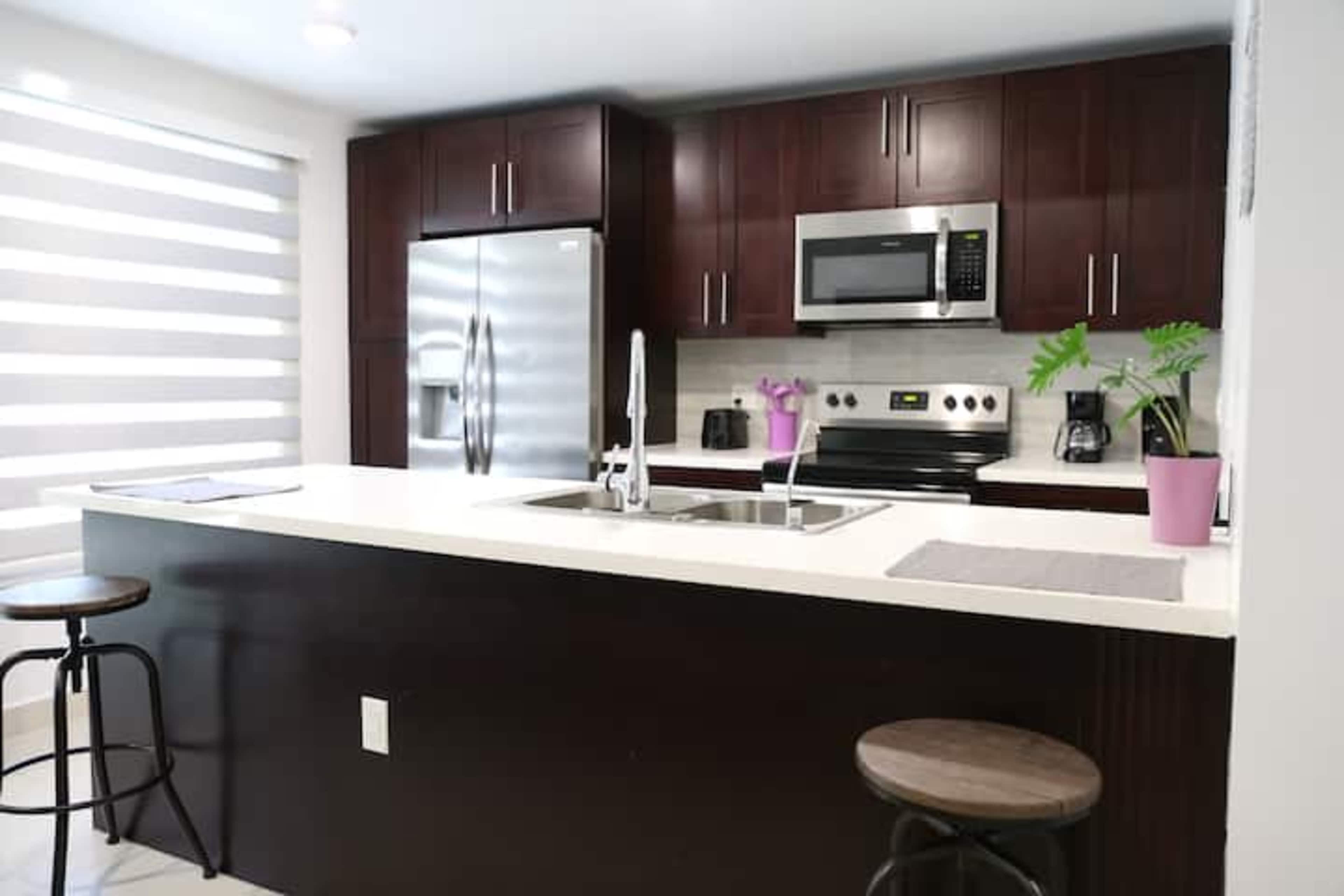 A modern kitchen features dark wood cabinetry, stainless steel appliances, and a central island with bar stools.