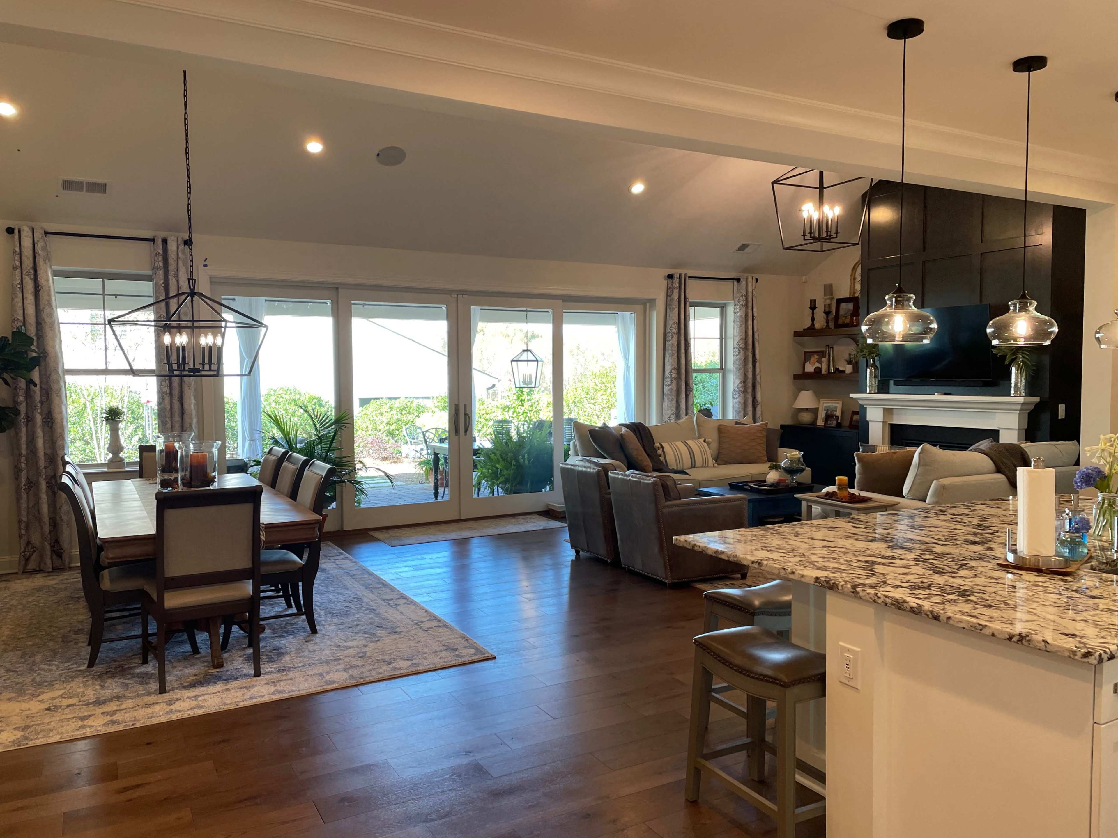A modern open-concept living space with a dining area, kitchen, and sitting area, featuring large windows and contemporary furnishings.