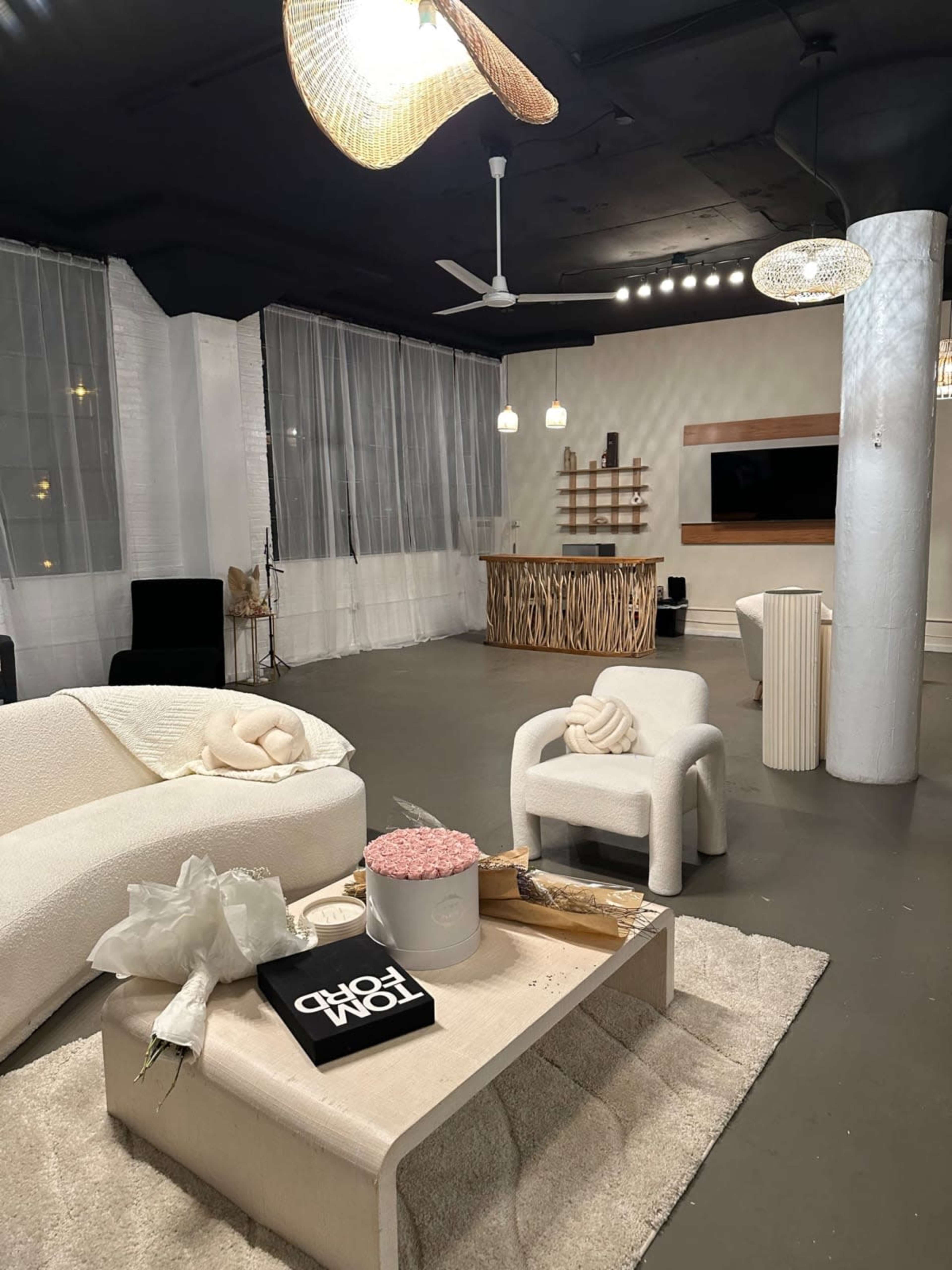 The image depicts a modern, minimalist living space featuring a light-colored sofa, decorative elements on a coffee table, and a wooden feature wall with a television.