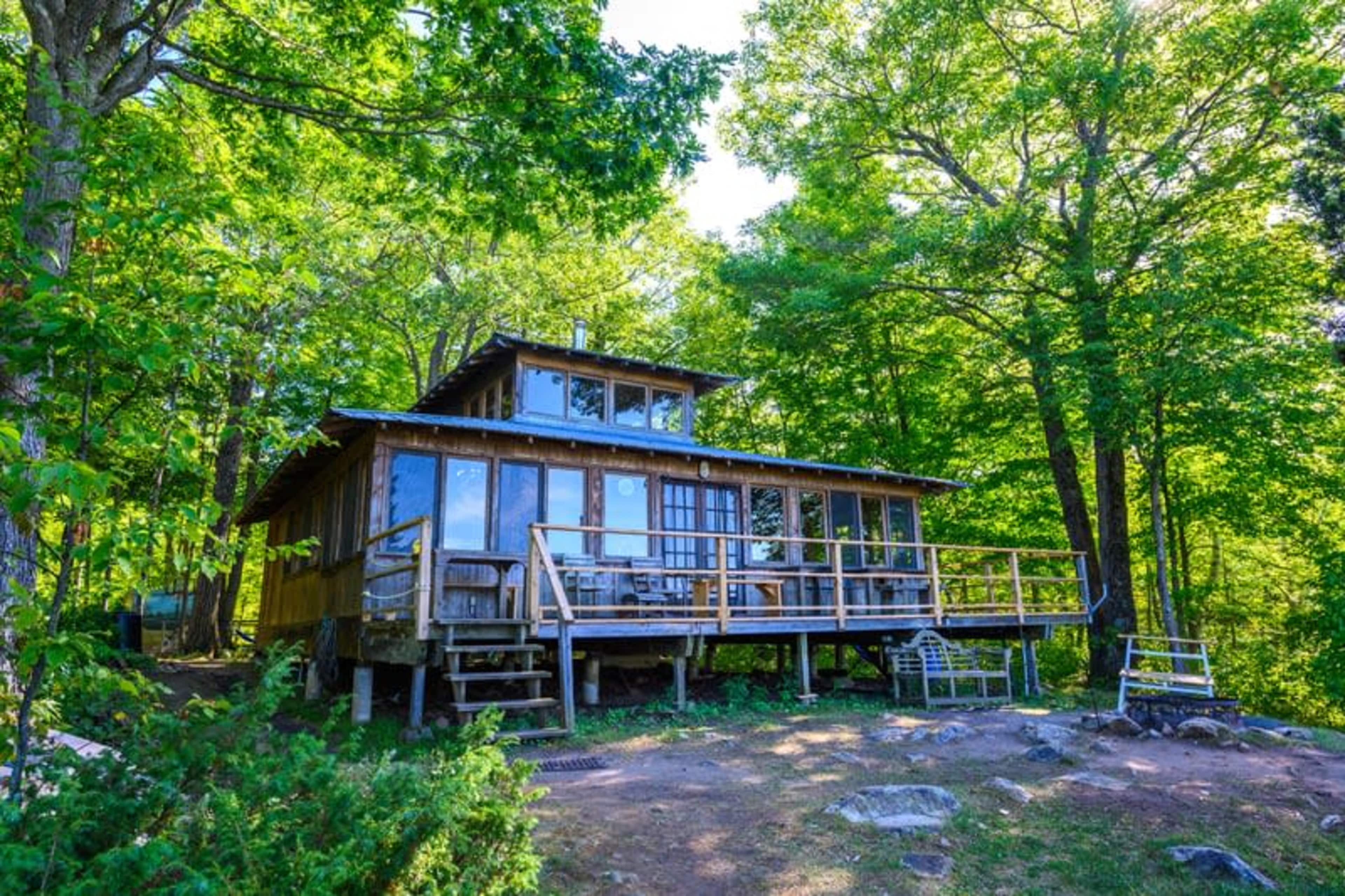 A wooden cabin with large windows is situated on a hillside surrounded by green trees.