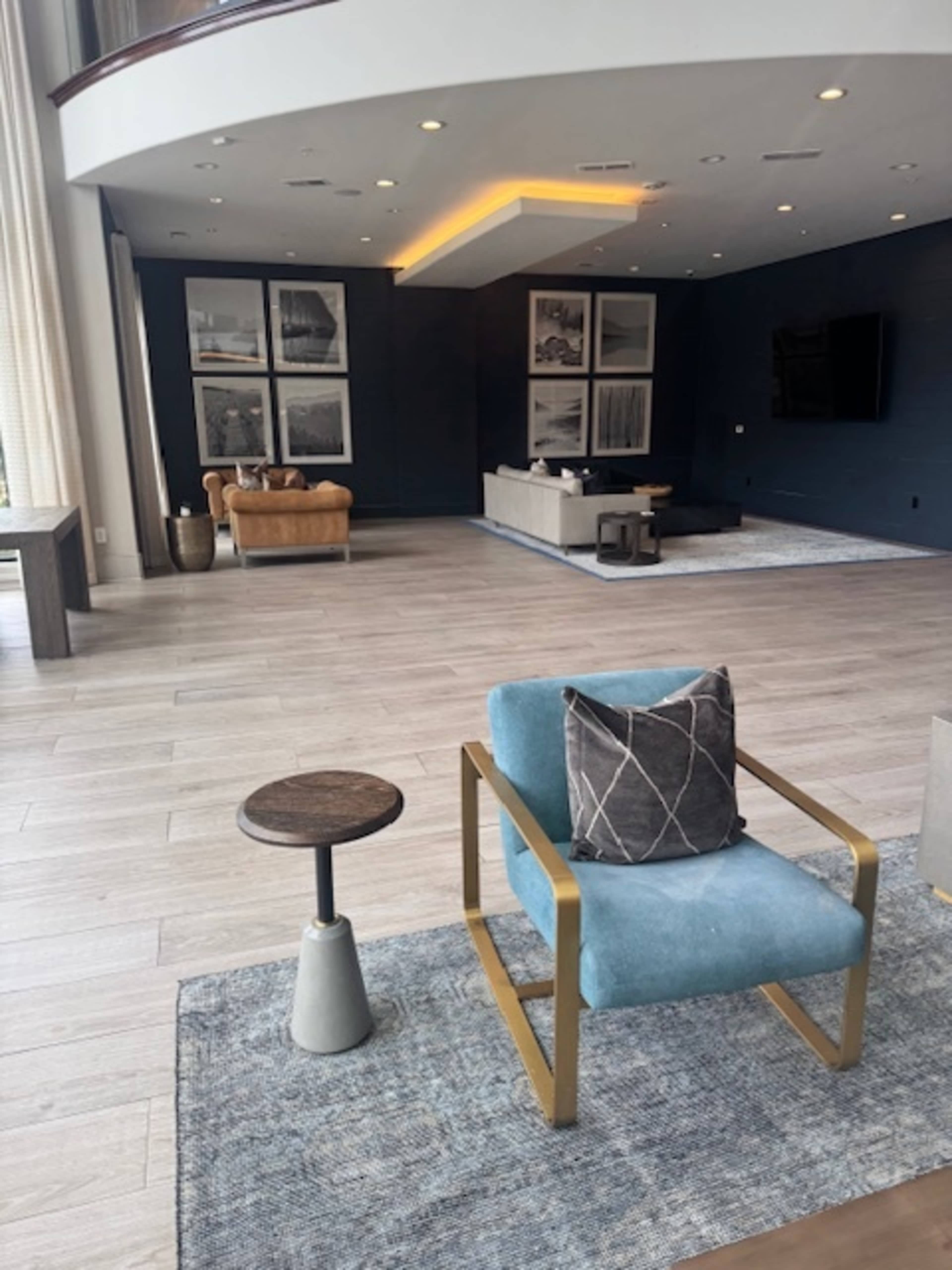 The image shows a modern living space with a blue accent chair and a small side table, featuring large windows and framed artwork on the walls.