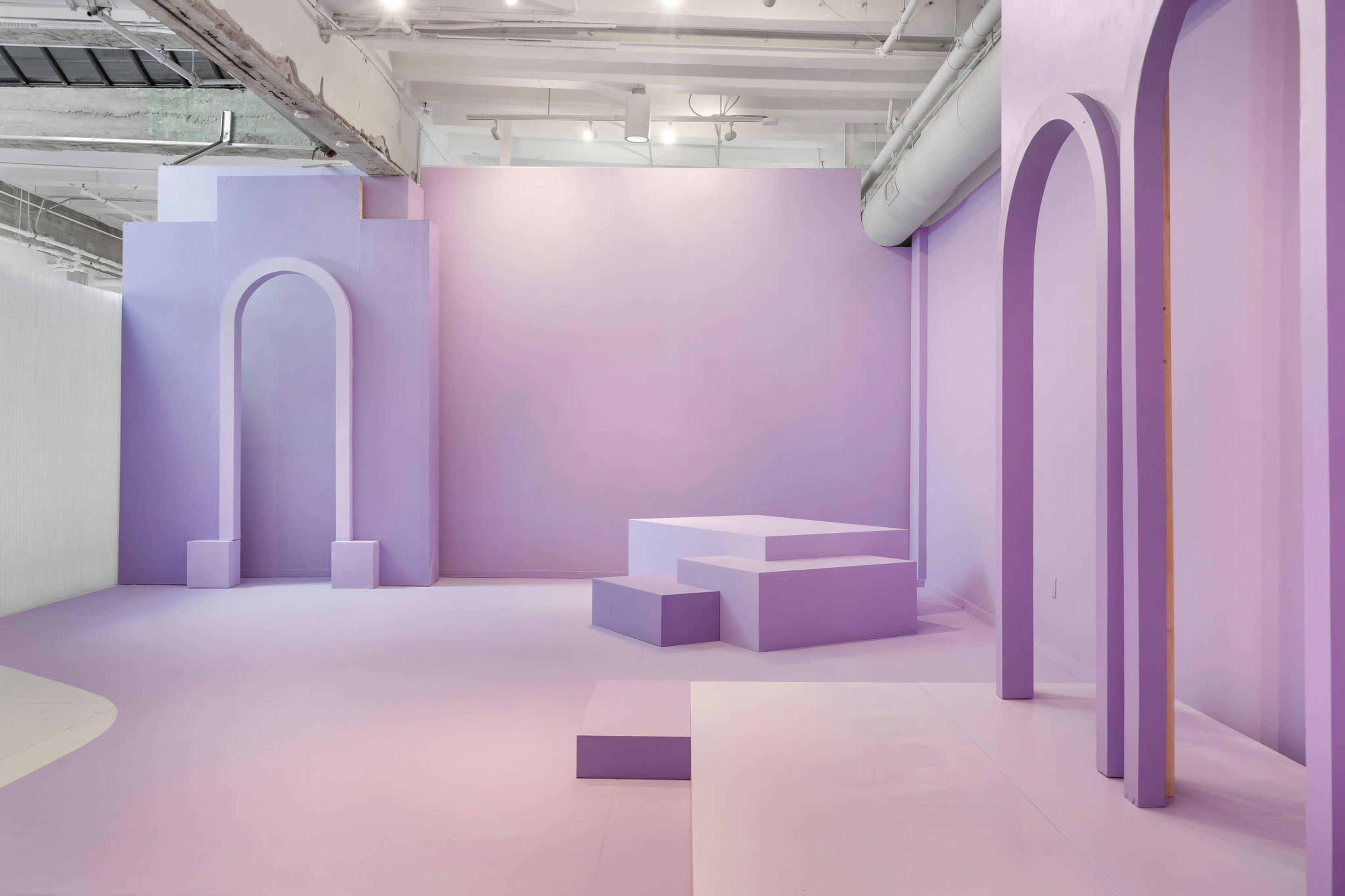 A minimalist interior space featuring various geometric structures and arched openings, all in shades of lavender.