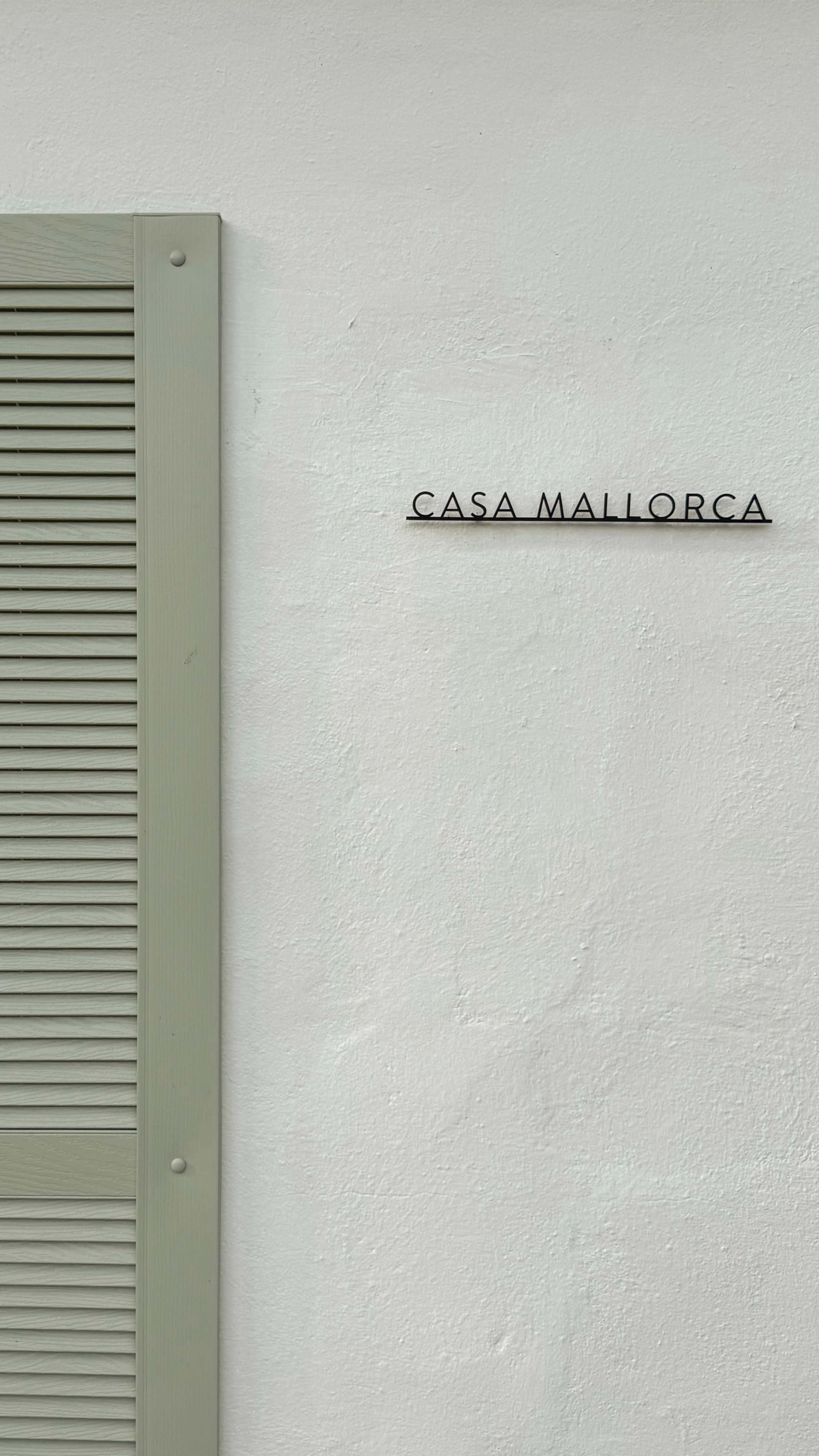 The image features a white wall with the words "CASA MALLORCA" displayed above a green shutter.