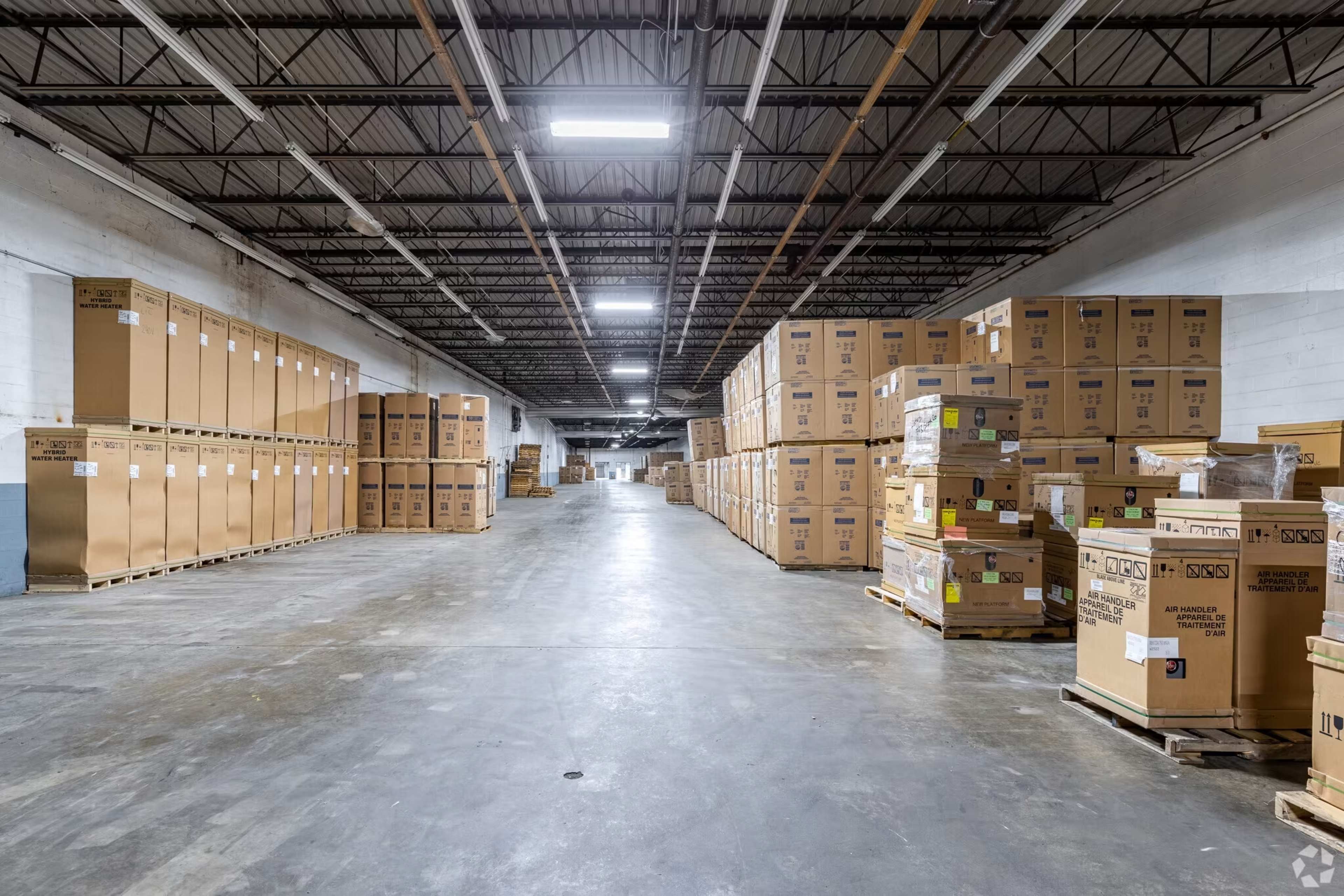 A spacious warehouse interior with tall stacks of cardboard boxes and pallets lined along the aisles.
