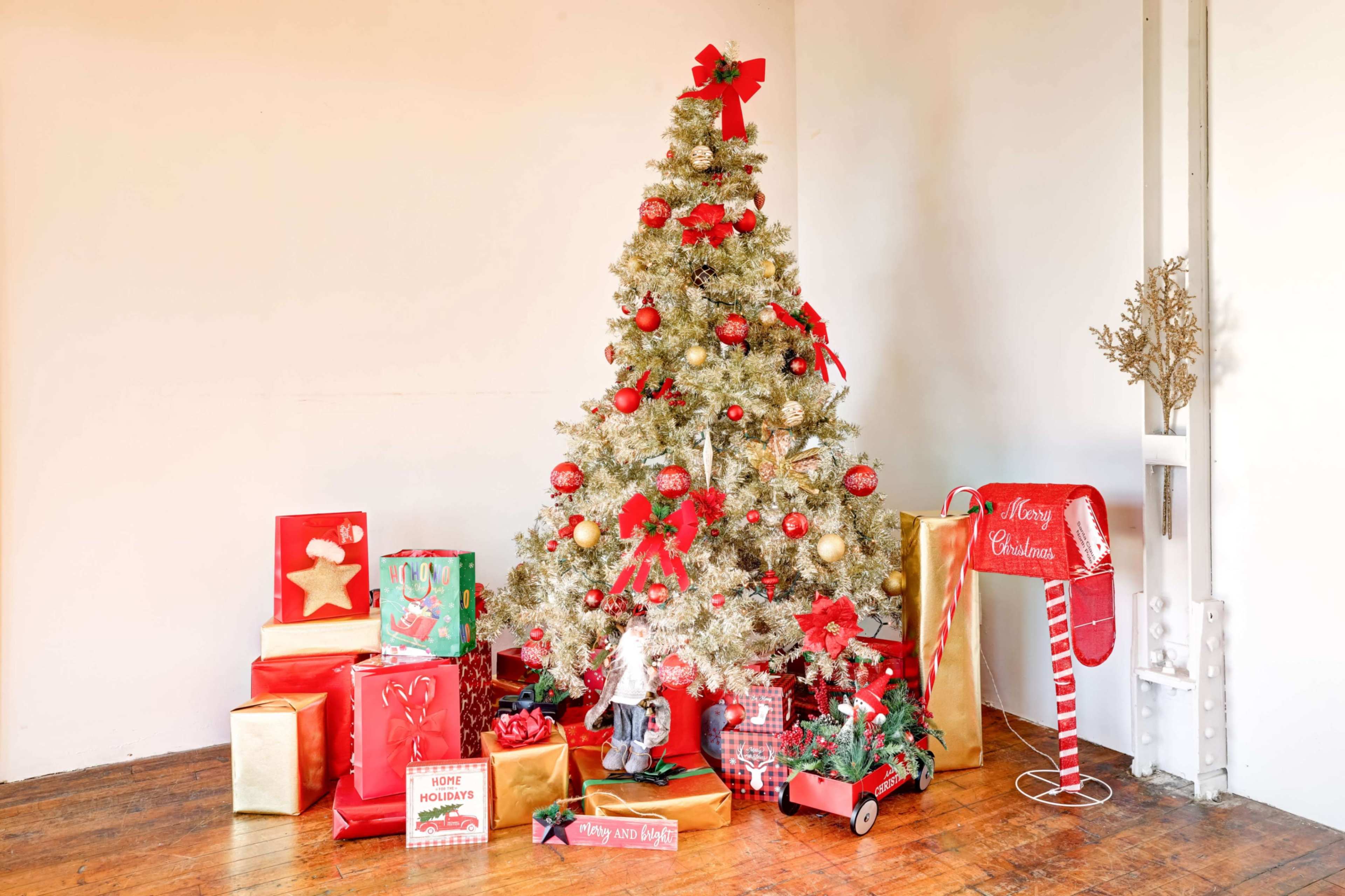 The scene features a decorated Christmas tree with red and gold ornaments, surrounded by an assortment of colorful gift boxes and a festive mailbox.