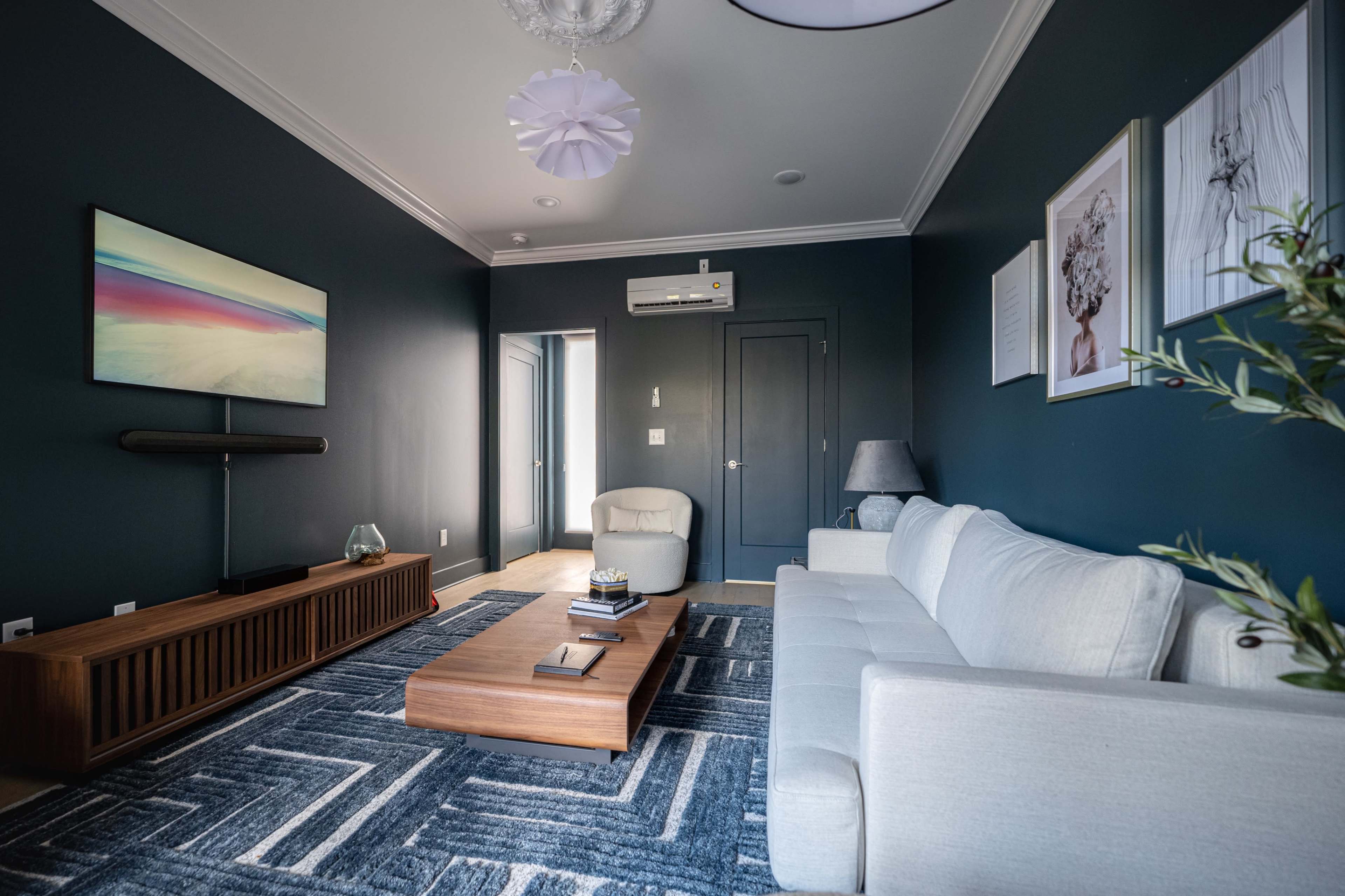 The living room features a gray sofa, a wooden coffee table, and a large wall-mounted television against a dark blue wall.