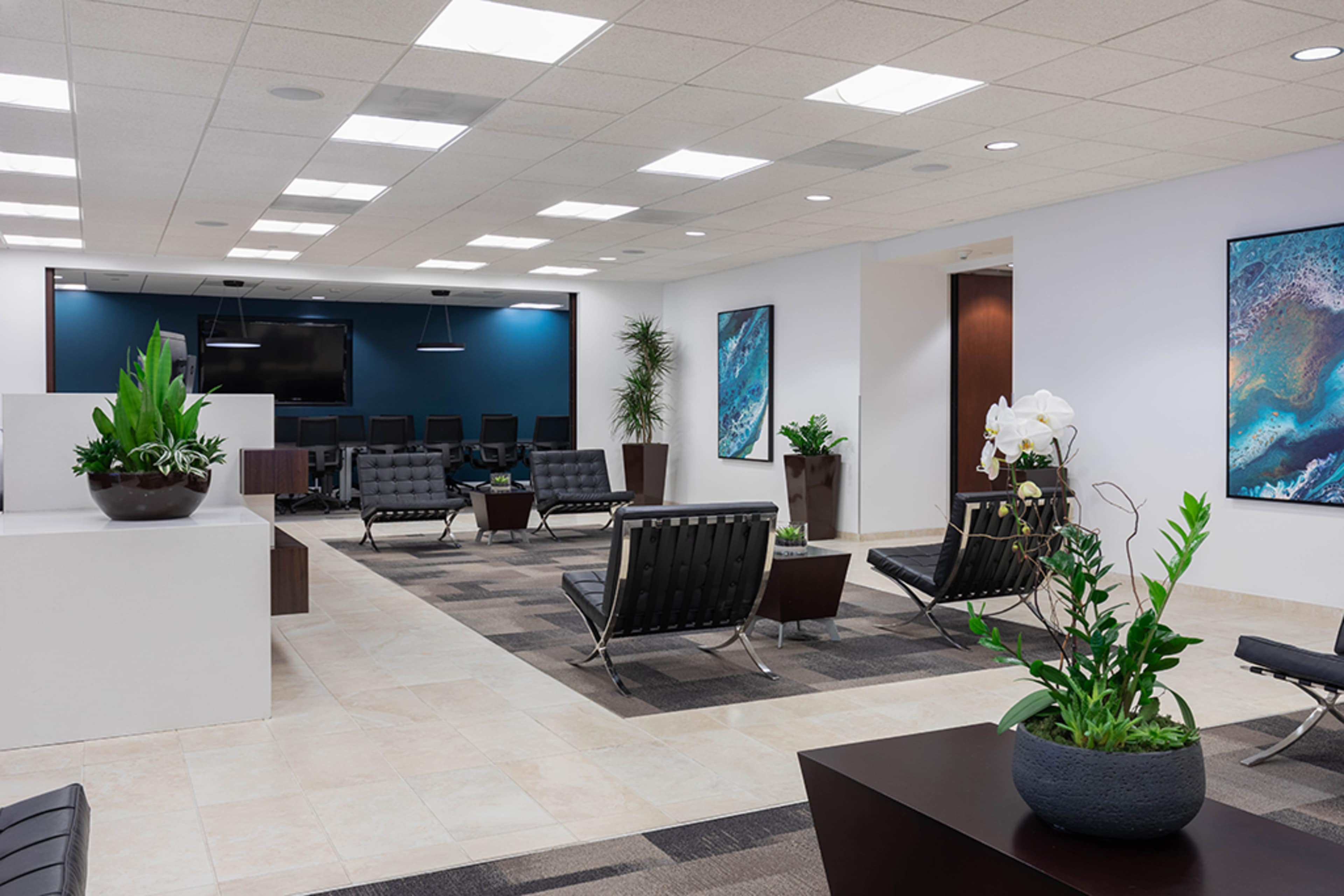 The image shows a modern office lobby with black leather seating, potted plants, and computer stations in the background.