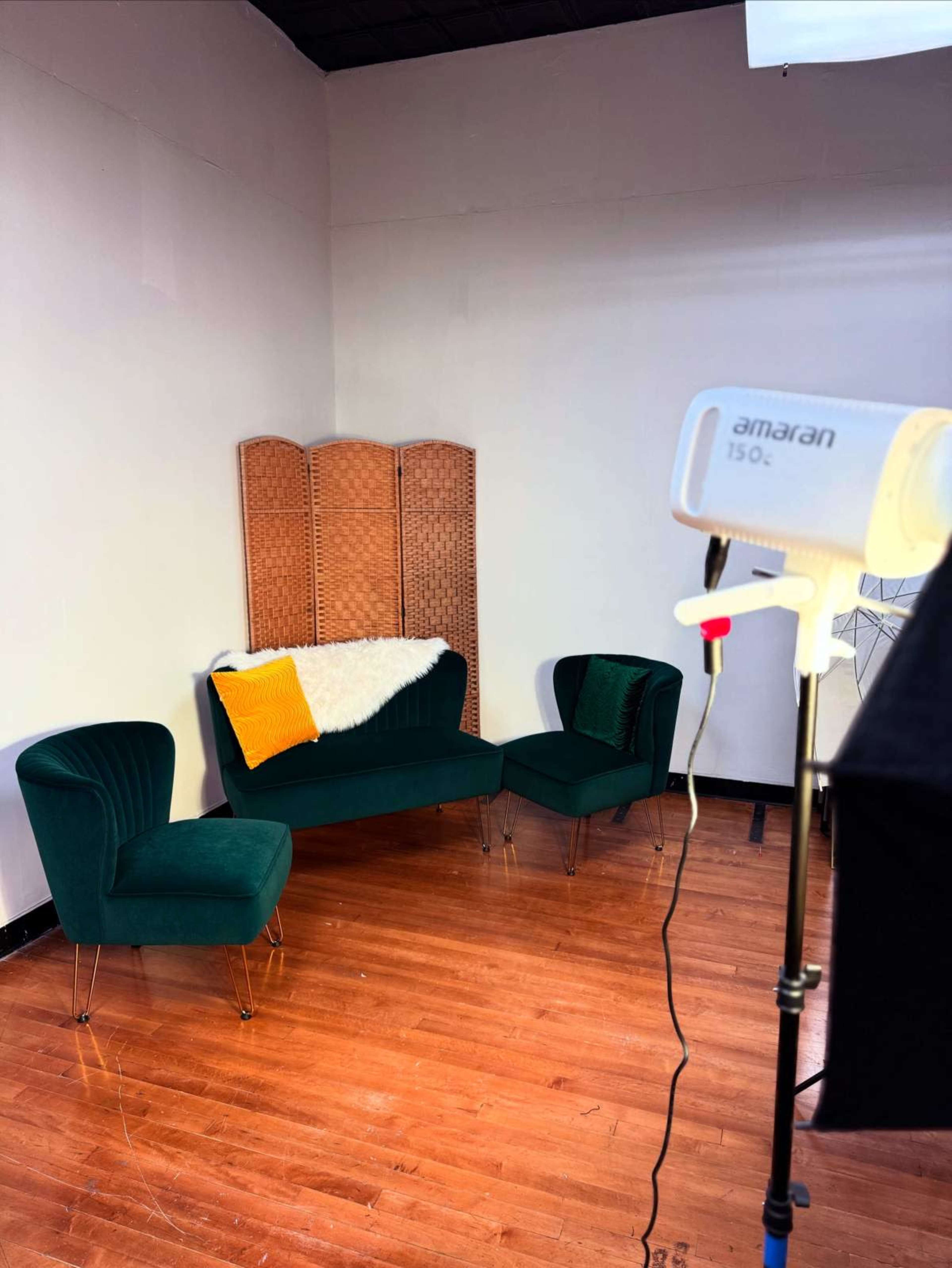 The image features a cozy seating arrangement with two green velvet chairs and a green couch, paired with a wicker room divider and illuminated by a soft light source.