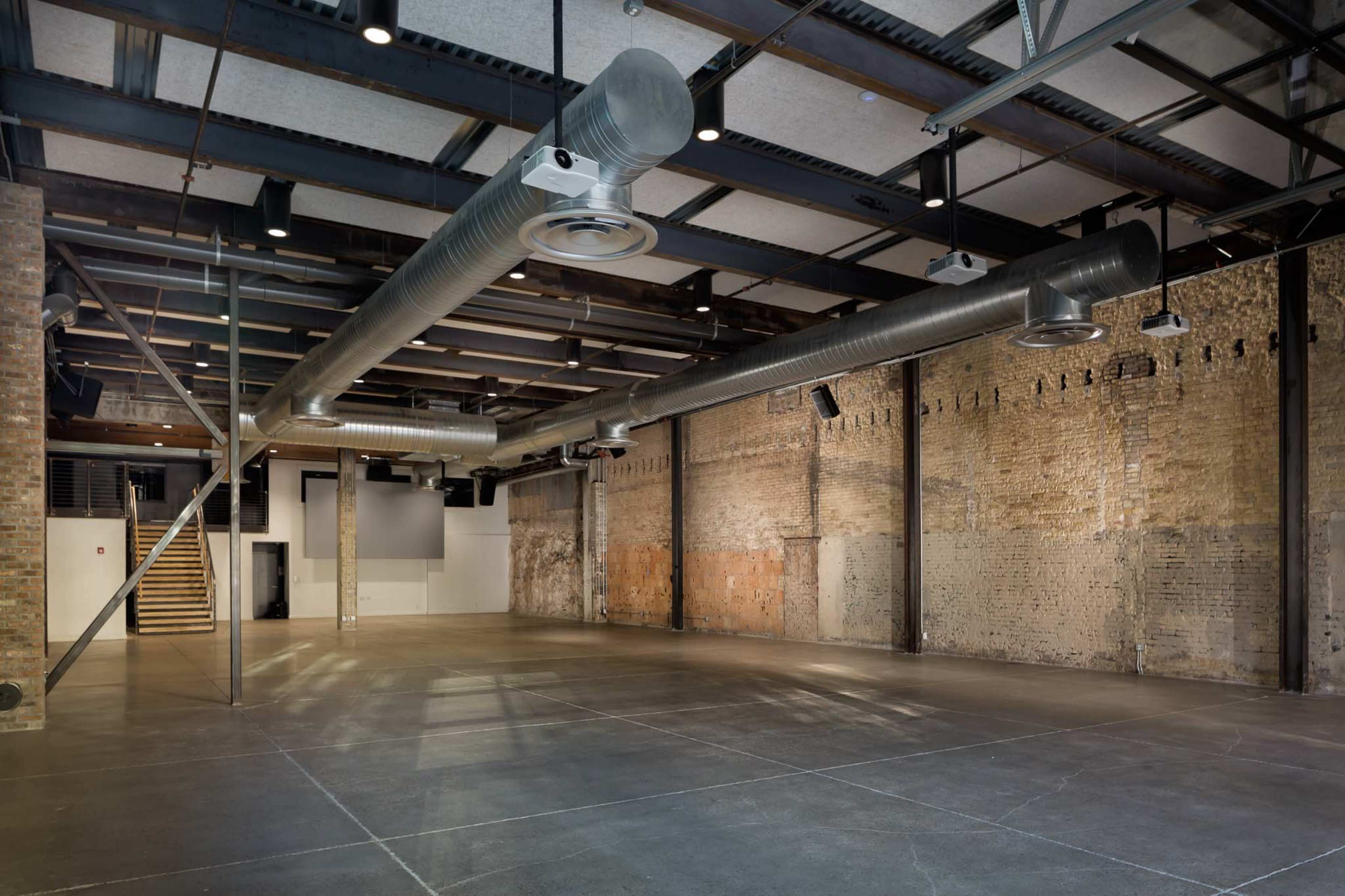 An open, industrial-style event space with exposed brick walls and large metal ventilation ducts.